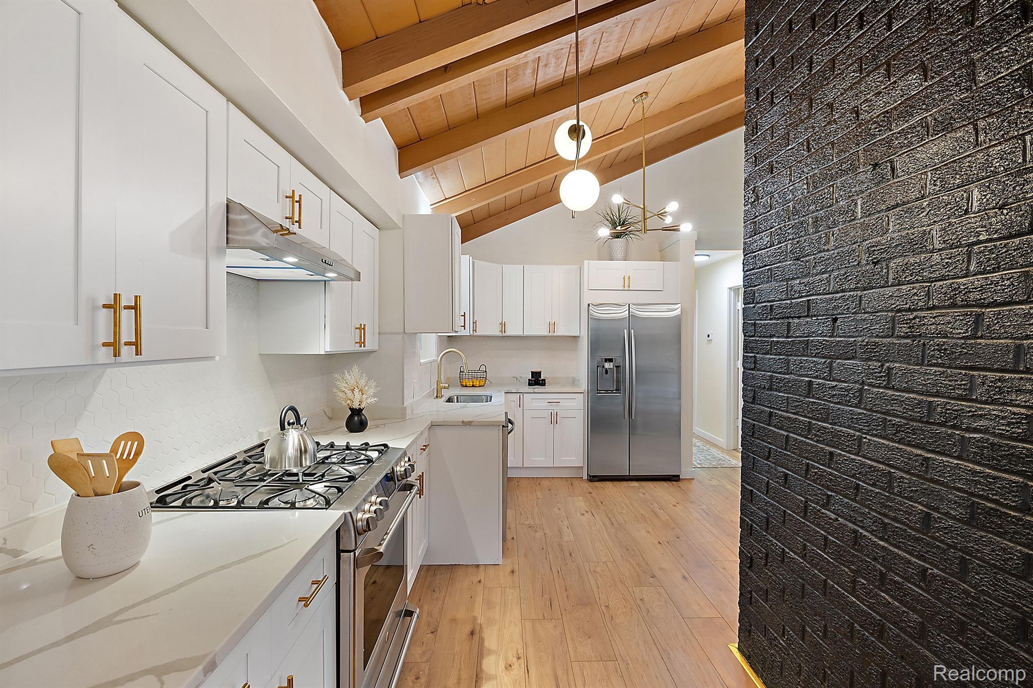 Kitchen with white cabinets, stainless appliances, a vaulted wood-beam ceiling, and a black brick accent wall.