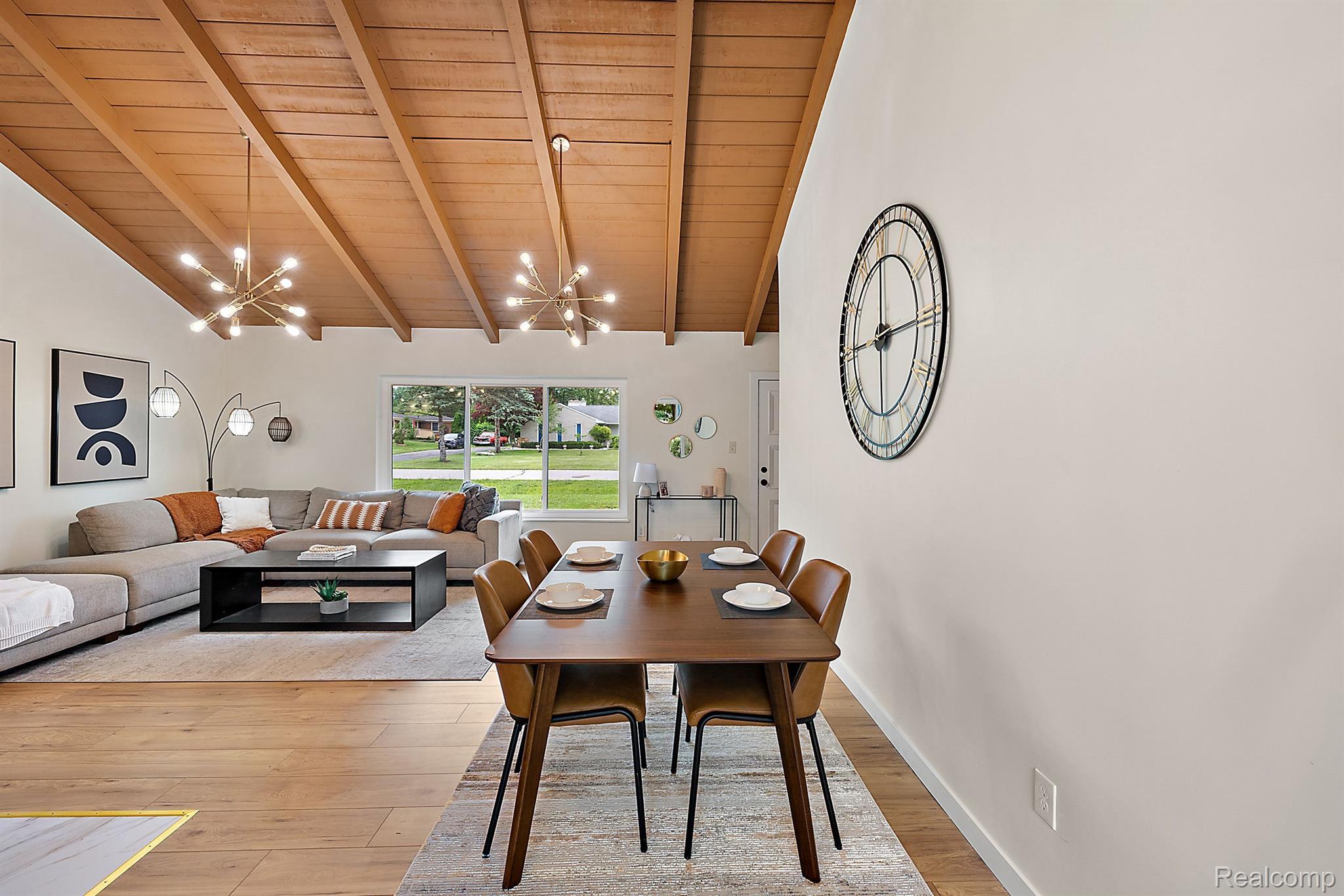 Open-plan living and dining room with a vaulted wood ceiling, gray sectional, and hardwood floors.