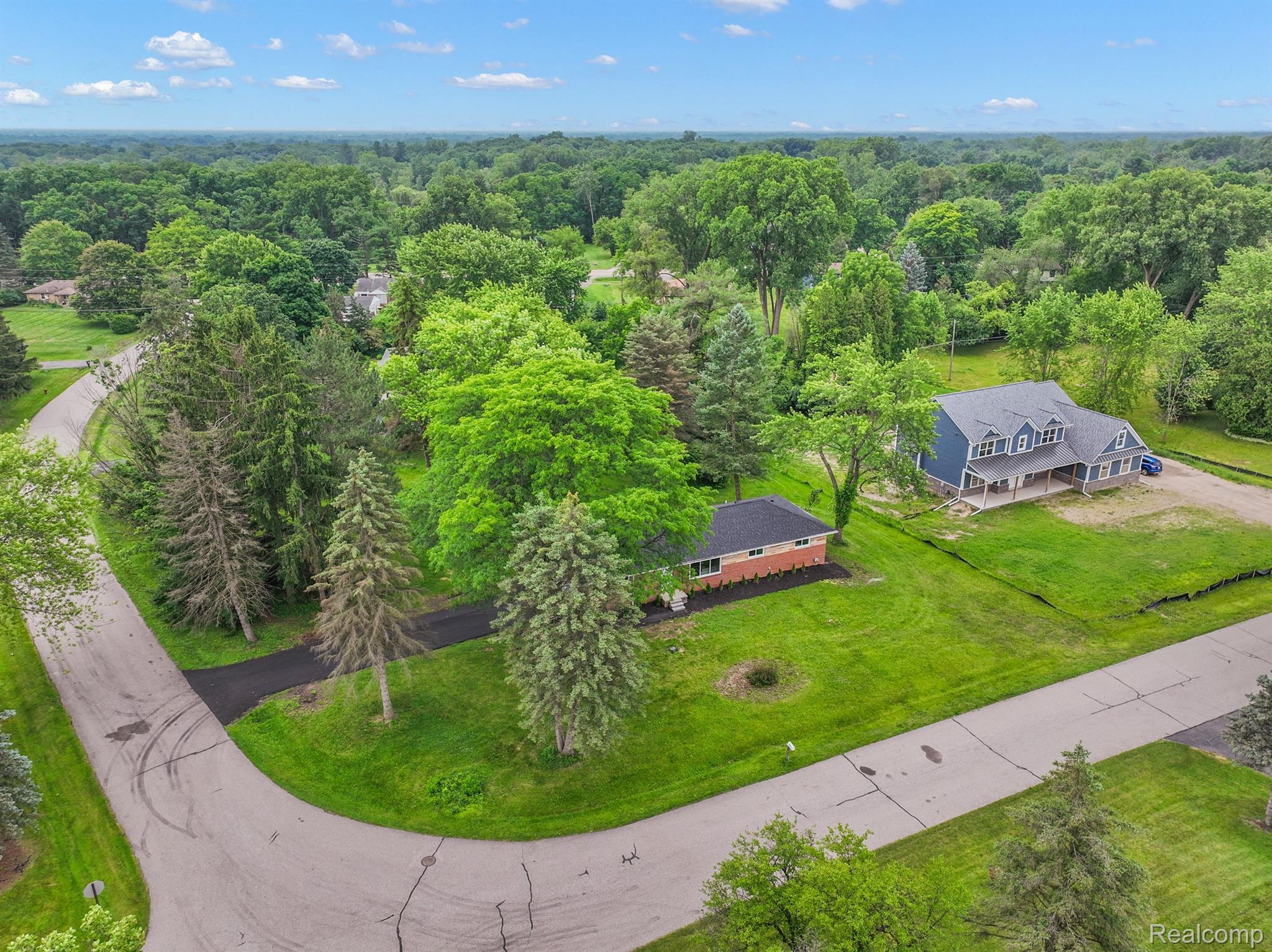 Aerial view of a gray multi-gabled home on a spacious, tree-filled lot beside a curved road.