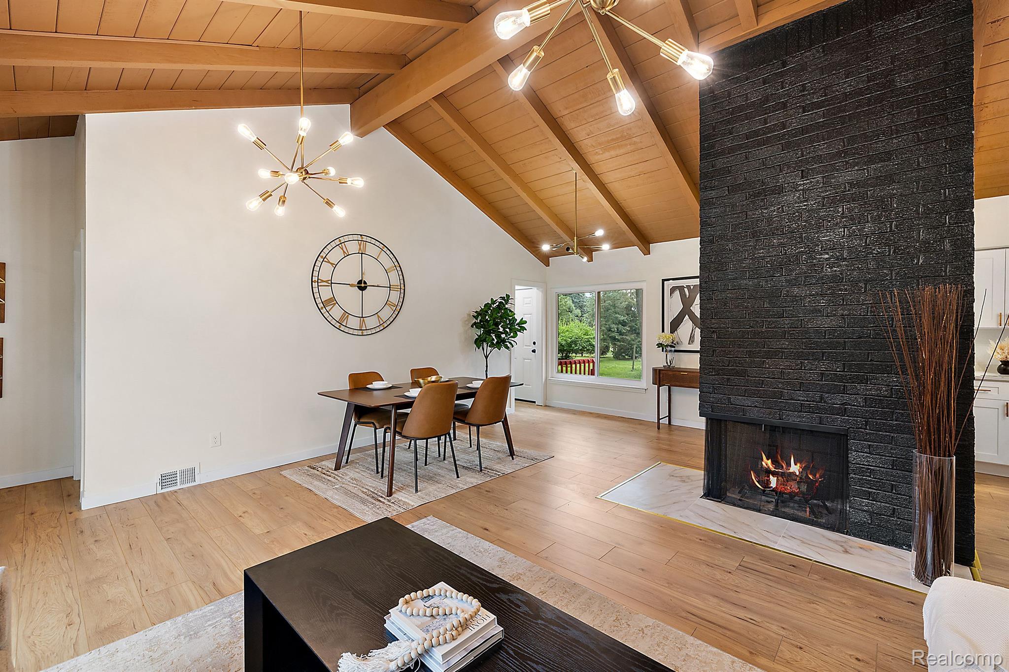 Open-plan living and dining room with a vaulted wood ceiling and tall black brick fireplace.