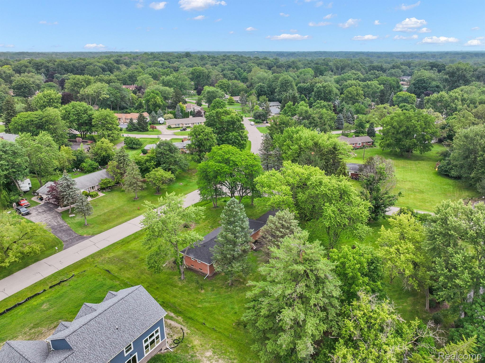 Aerial view of a home beside a tree-filled yard and quiet residential streets.