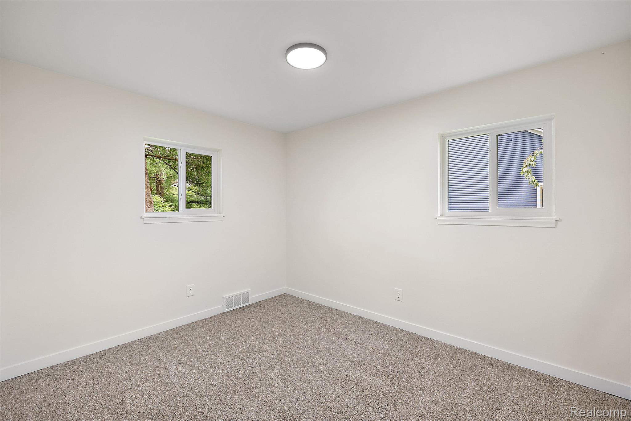 Empty carpeted room with two windows and a ceiling light.
