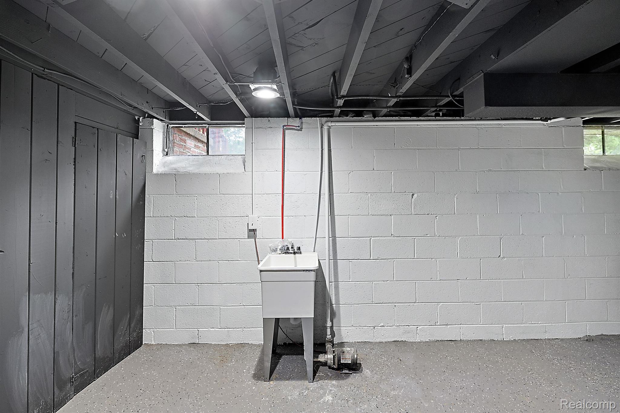 Unfinished basement utility area with a freestanding sink, exposed ceiling joists, and painted block walls.