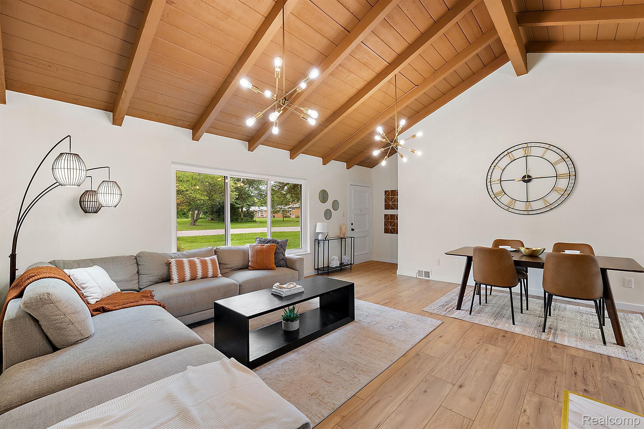 Open living and dining room with a vaulted wood ceiling, exposed beams, and large windows.