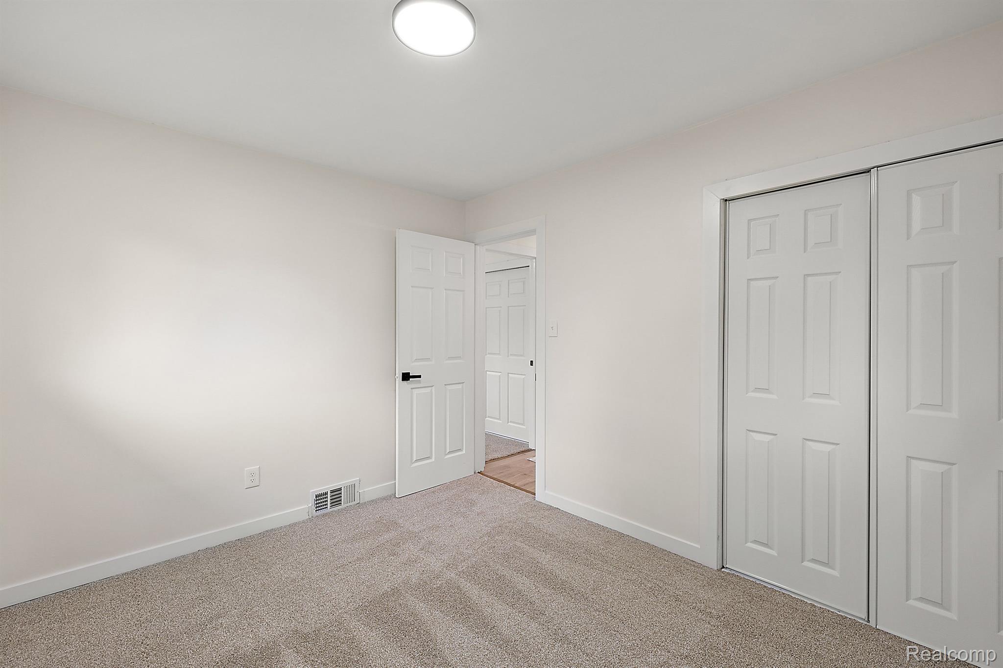 Empty carpeted bedroom with white sliding closet doors and an open doorway.