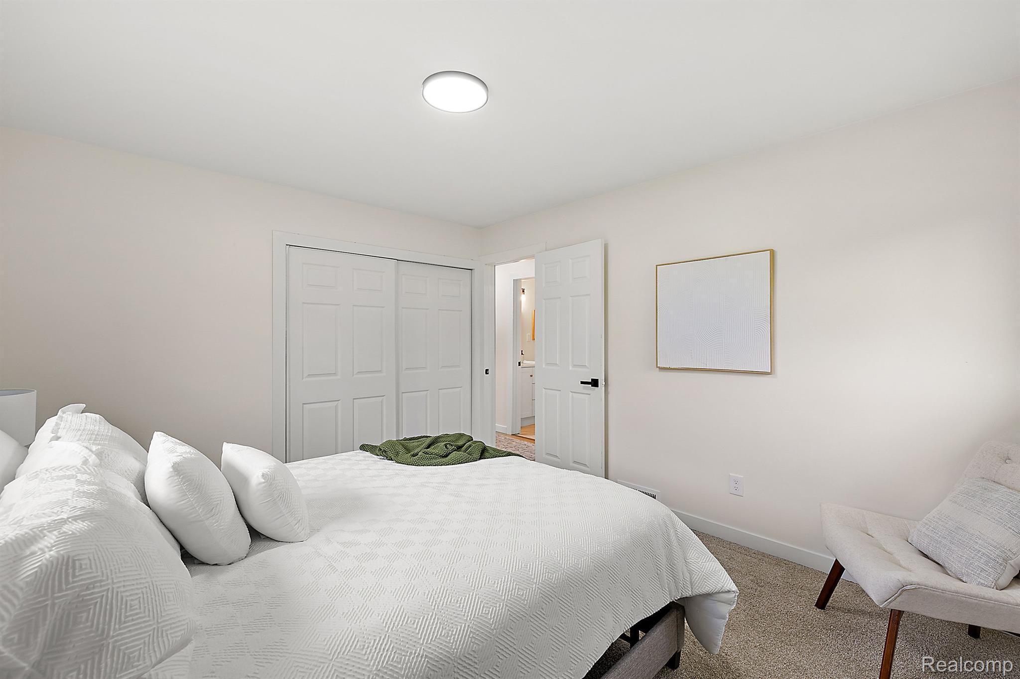 Staged bedroom with a white bed, sliding closet doors, and an open doorway.