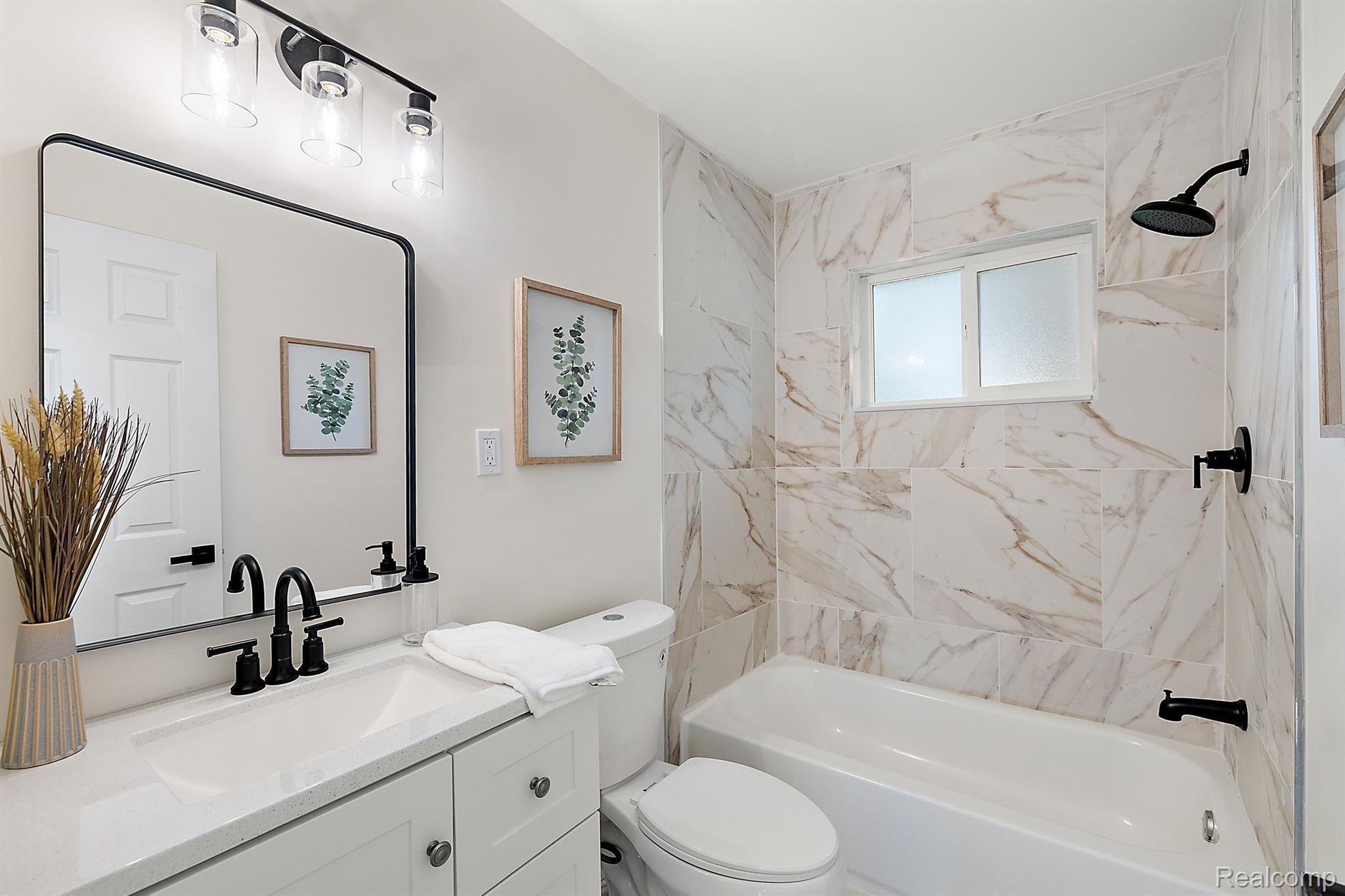 Bathroom with marble-look tile, a bathtub, white vanity, and matte-black fixtures.