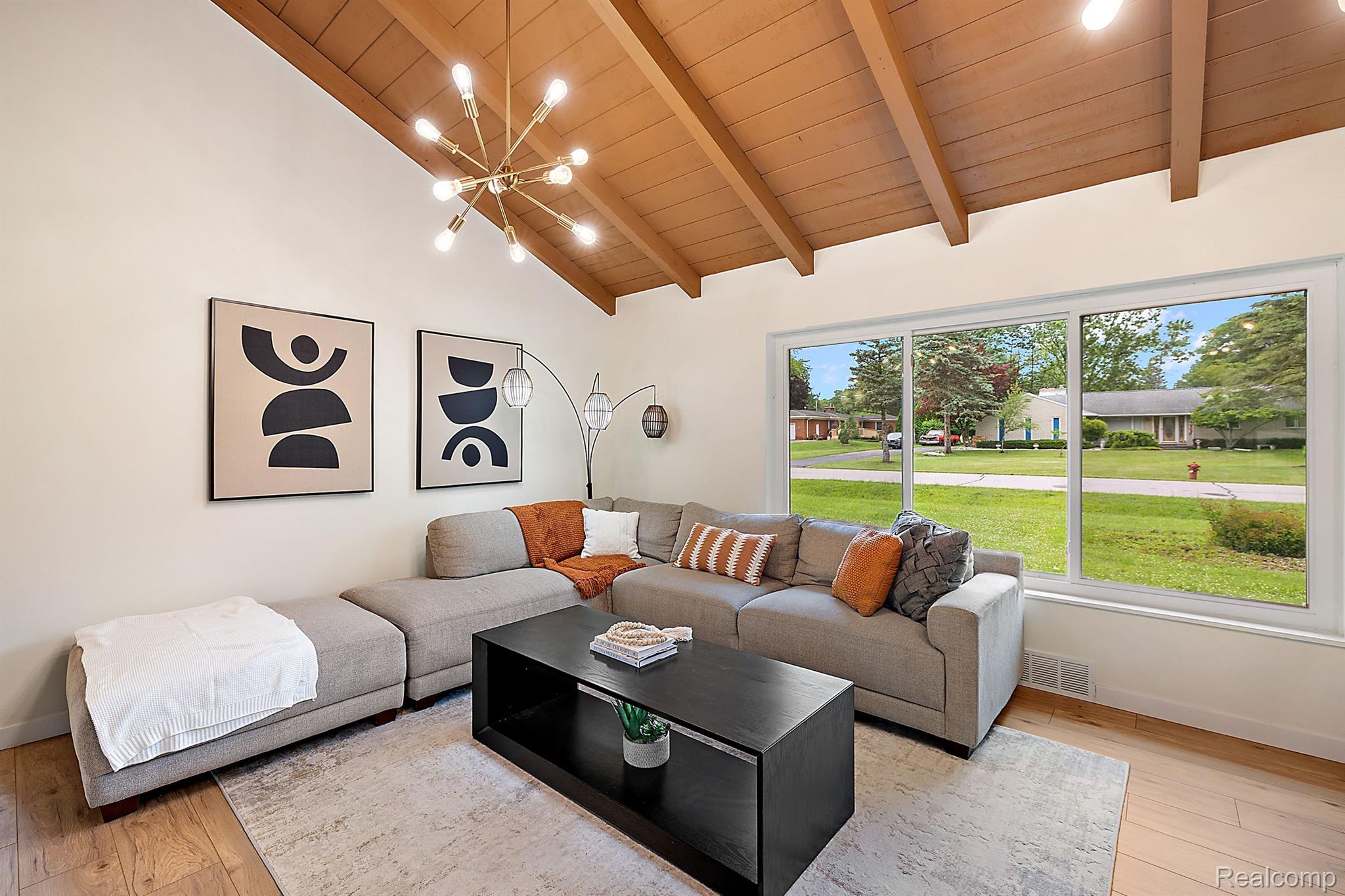 Living room with a gray sectional beneath a vaulted wood ceiling and a wide neighborhood-facing window.