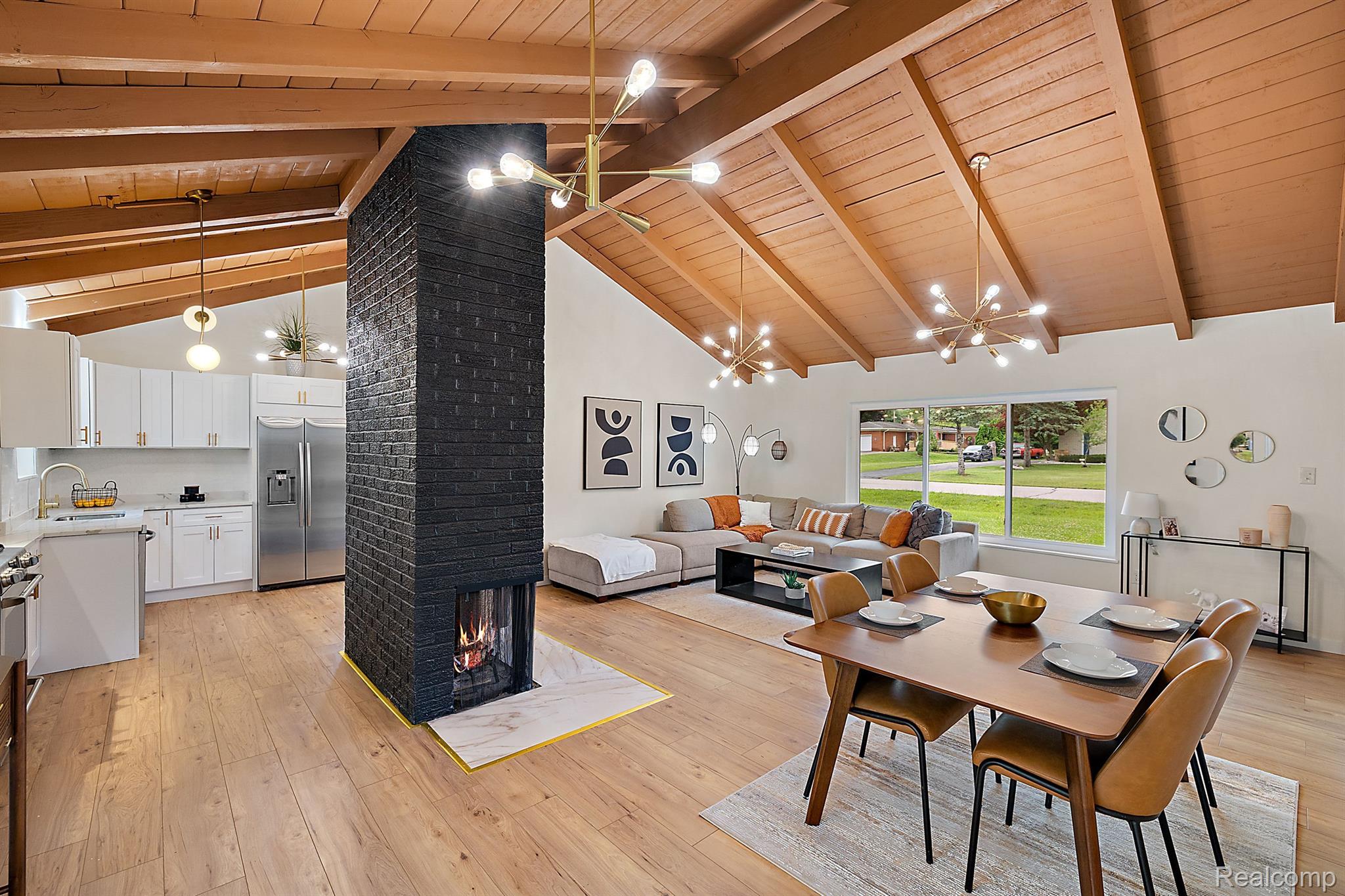 Open-plan living room and kitchen with a vaulted wood ceiling and central black brick fireplace.