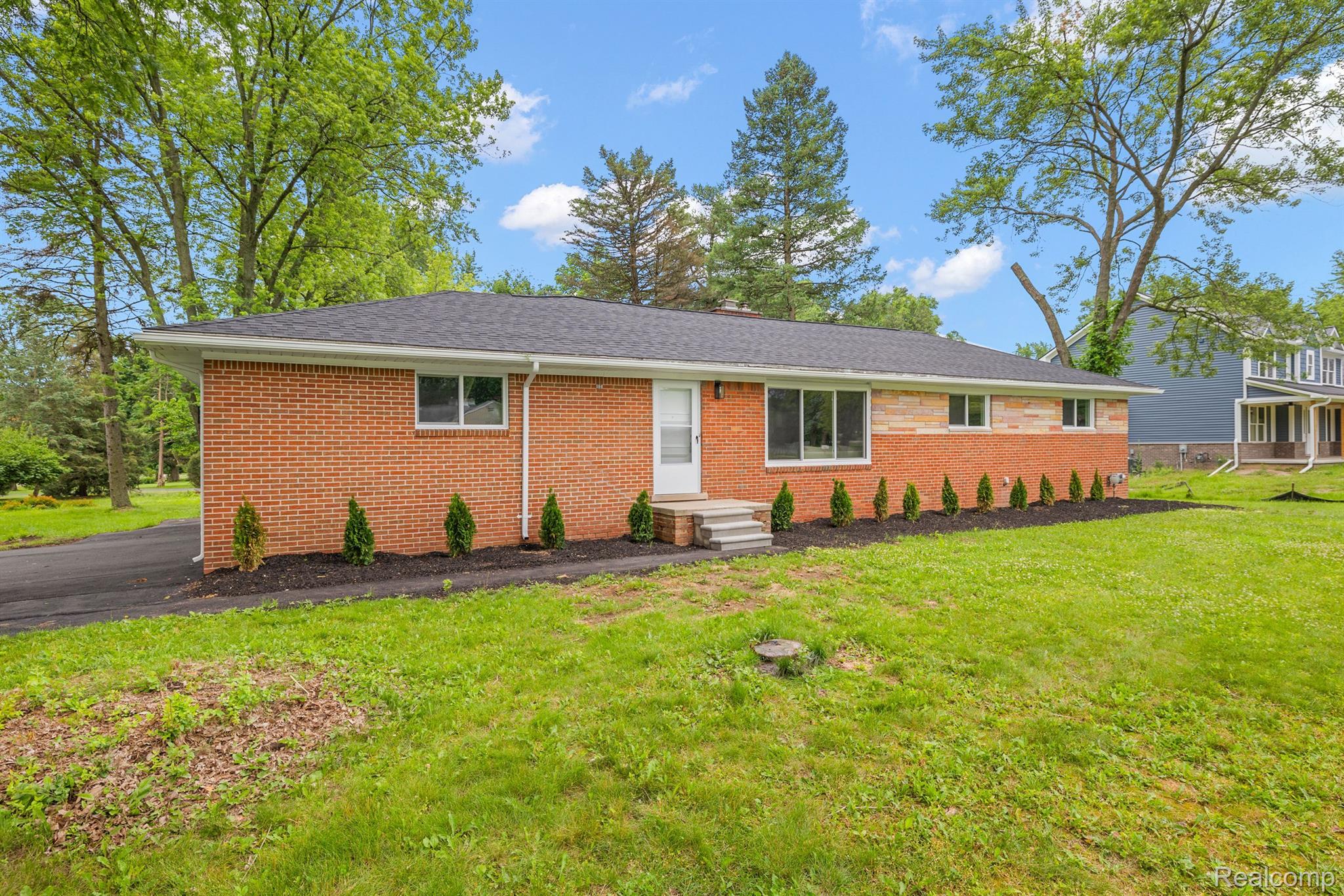 Red brick ranch home with a gray roof, front steps, and shrubs along the foundation.