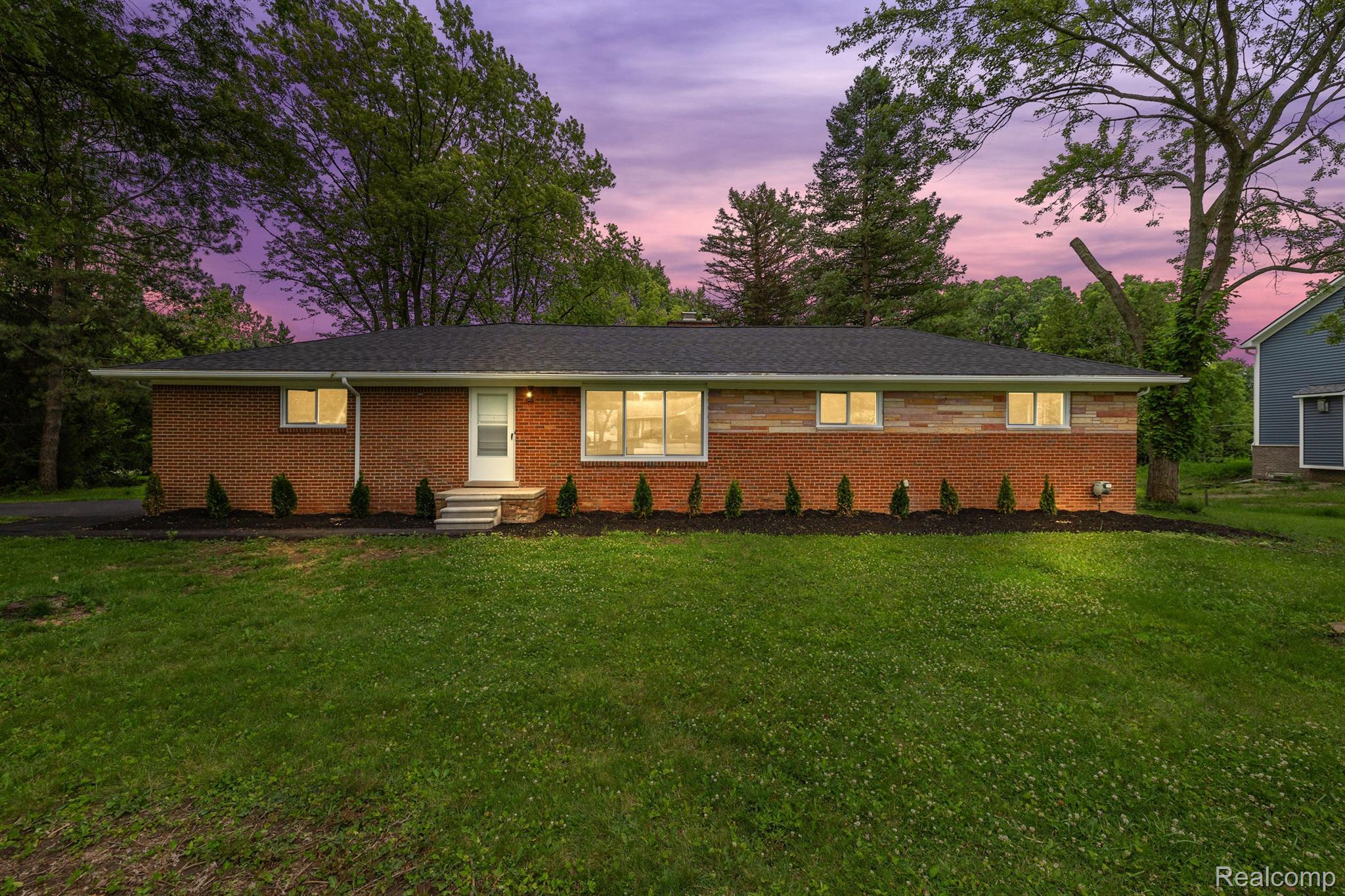 Red brick ranch home with a broad lawn and mature trees at dusk.
