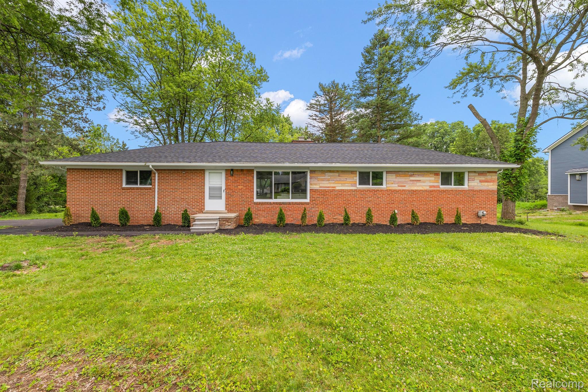 Single-story brick ranch house with stone accents, white entry steps, and a broad lawn.