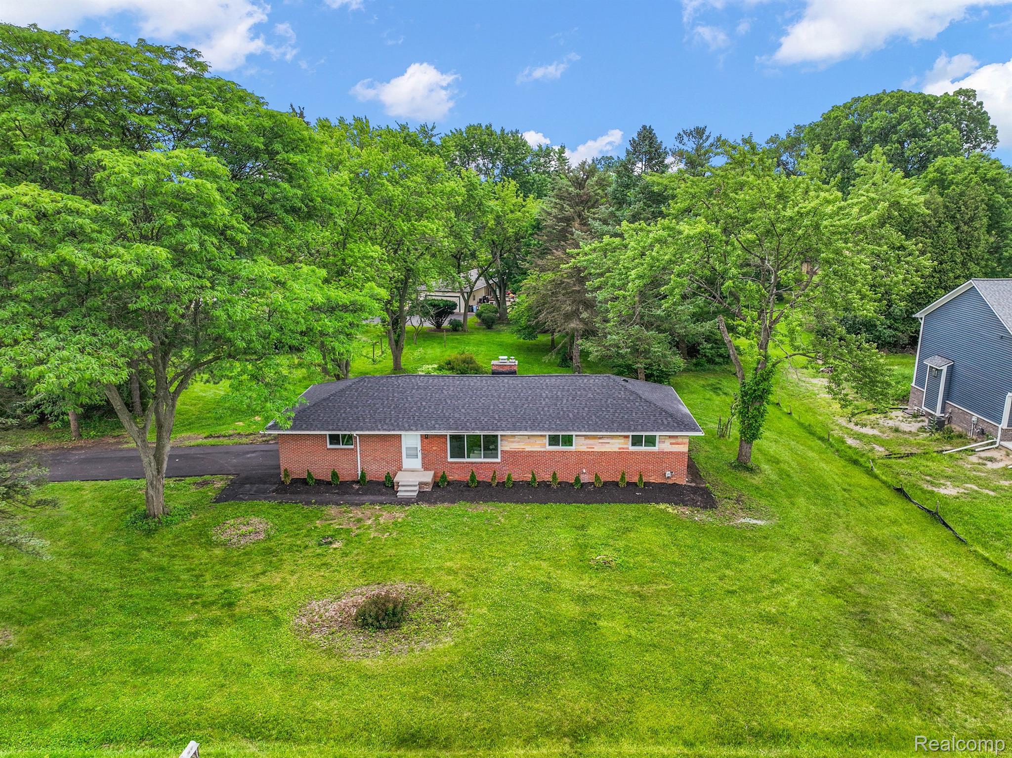 Aerial view of a brick ranch home surrounded by a broad lawn and mature trees.