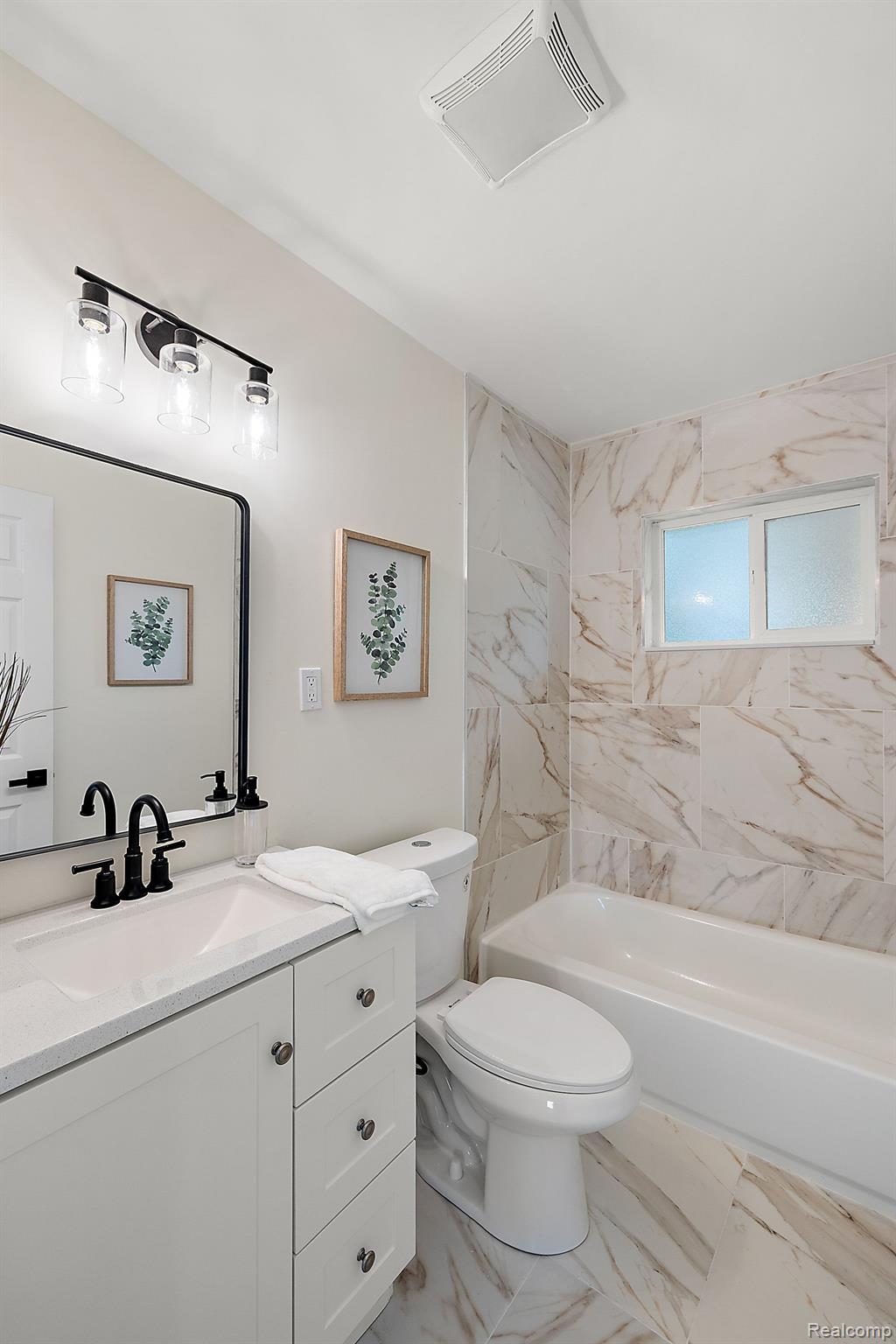 Renovated bathroom with a white vanity, black faucet, marble-look tile, and frosted window.