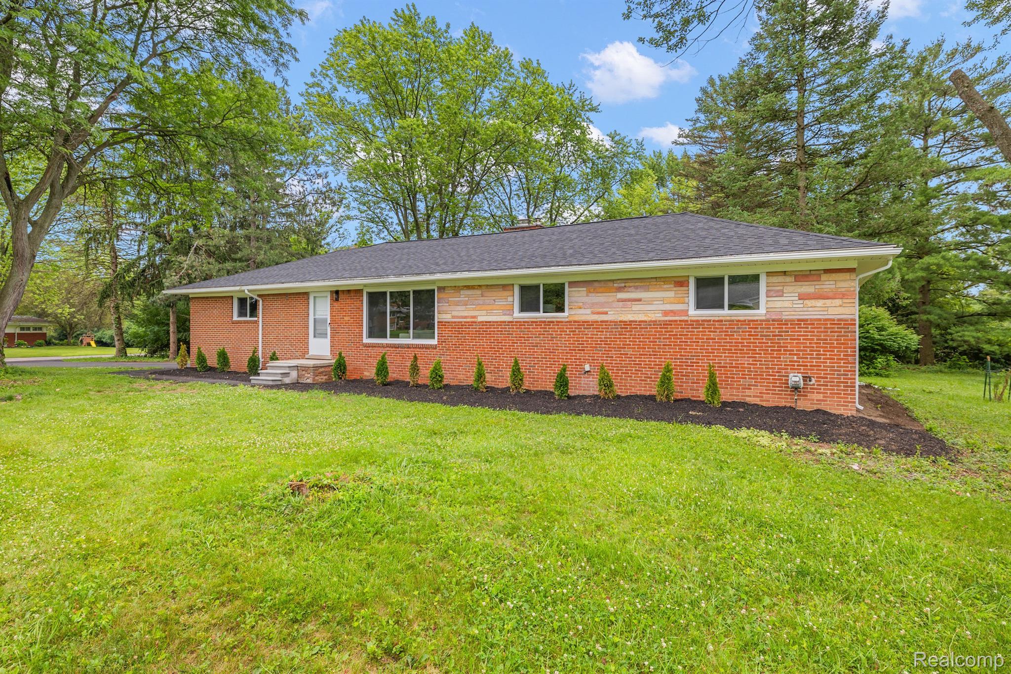 Single-story brick home with stone accents, a broad lawn, and mature trees.