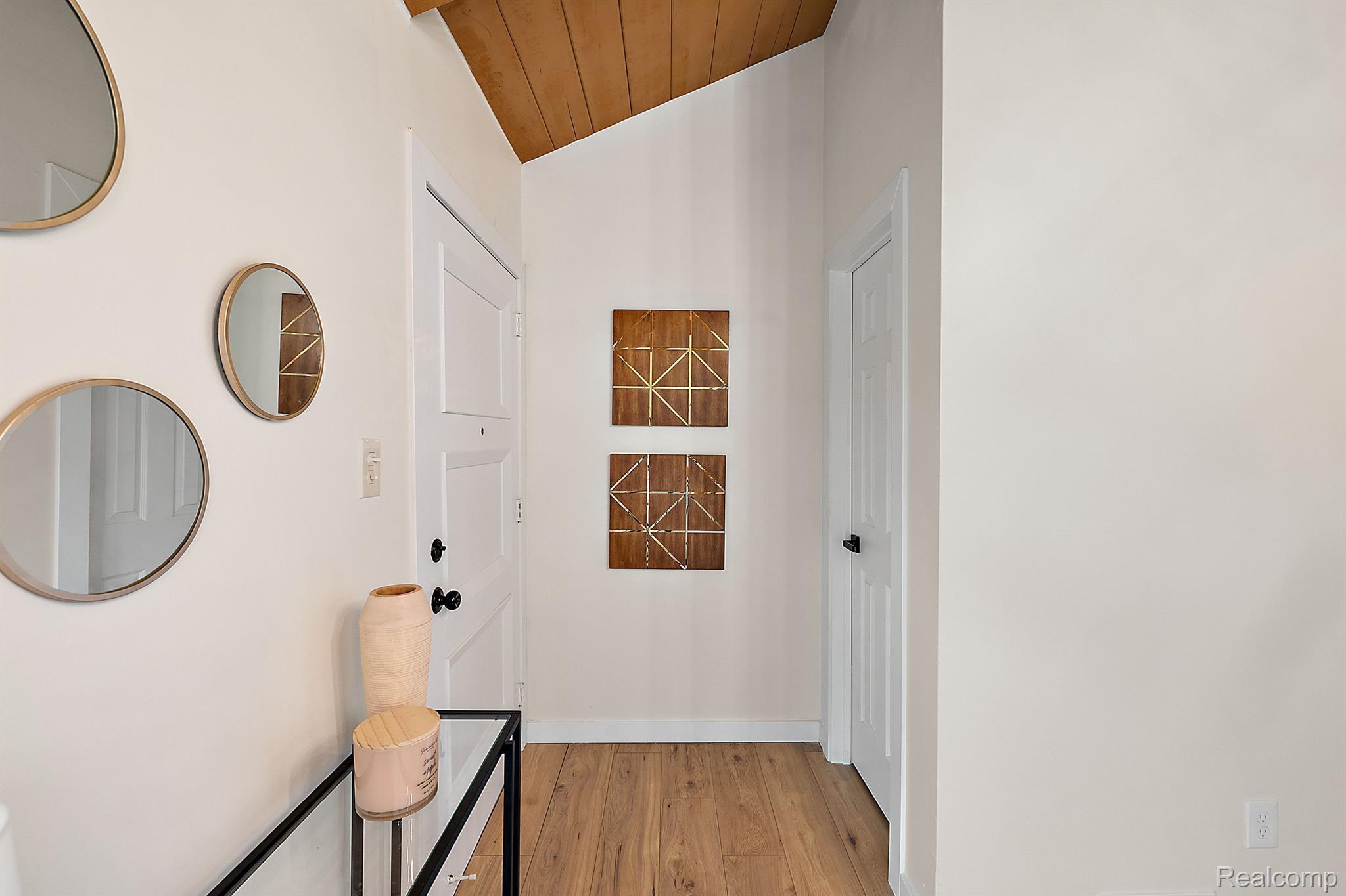 Entry foyer with vaulted wood ceiling, wood flooring, round mirrors, and geometric wall art.