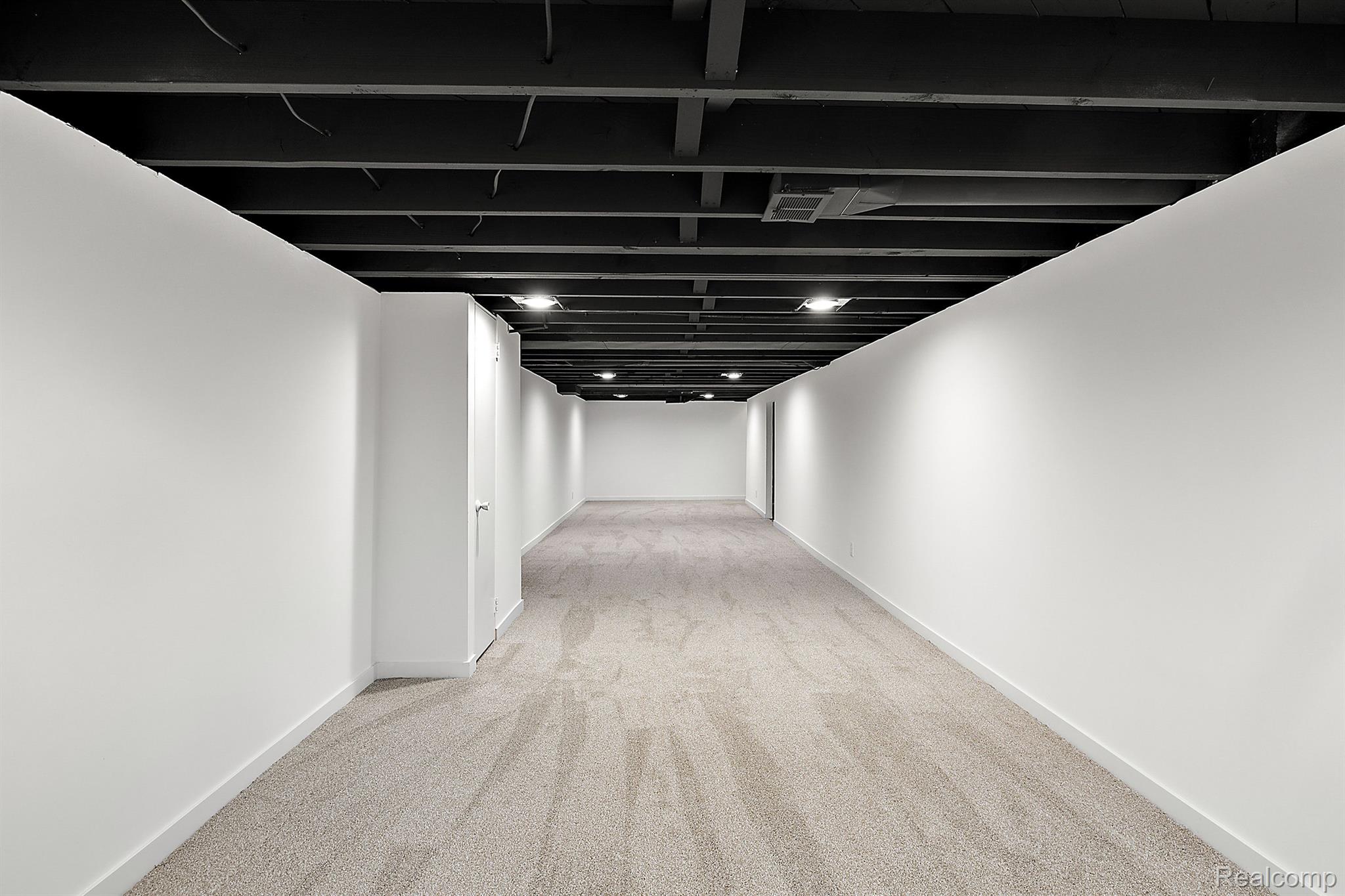 Vacant basement room with beige carpet, white walls, and an exposed ceiling.