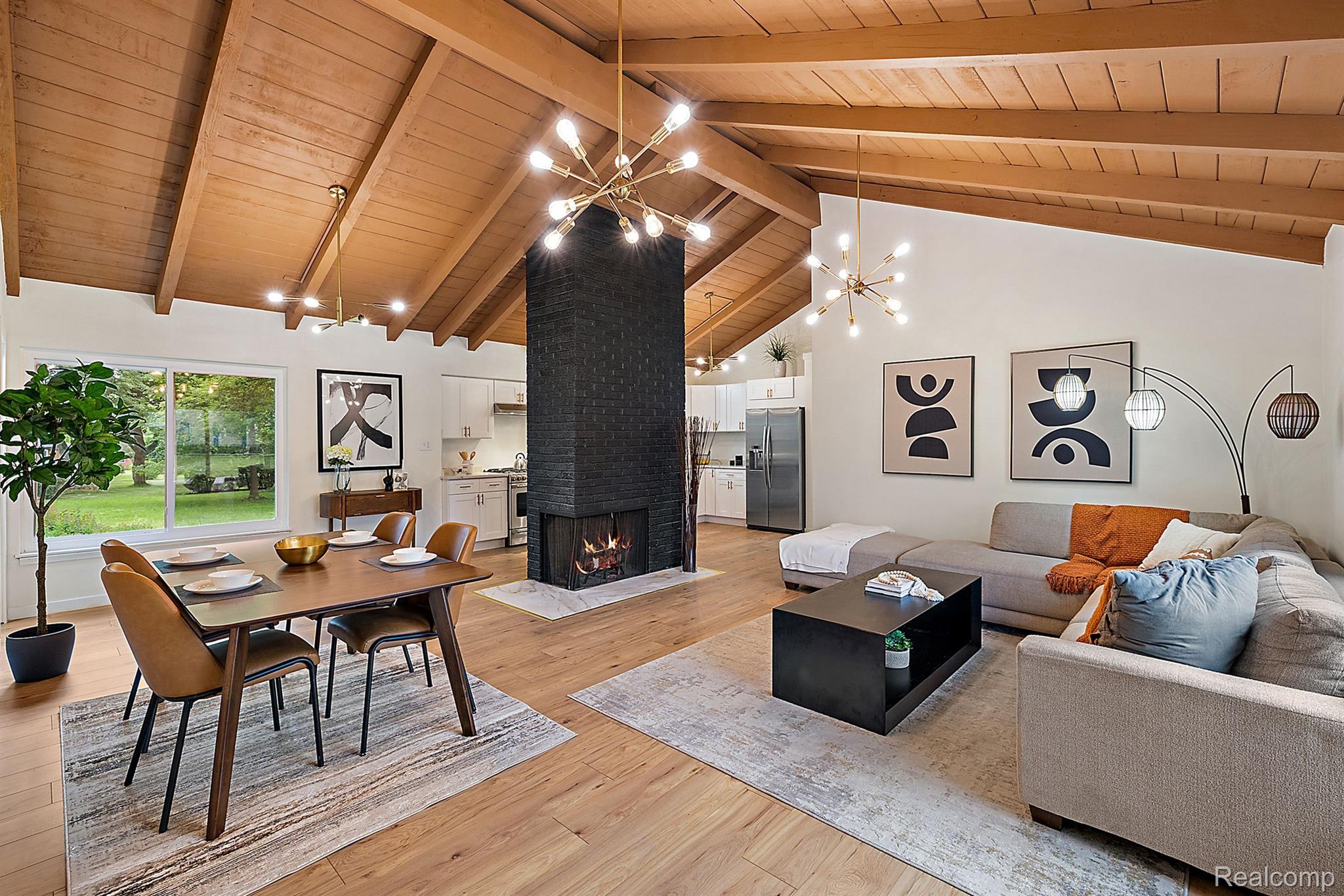 Open-plan living and dining room with a vaulted wood ceiling and central black brick fireplace.