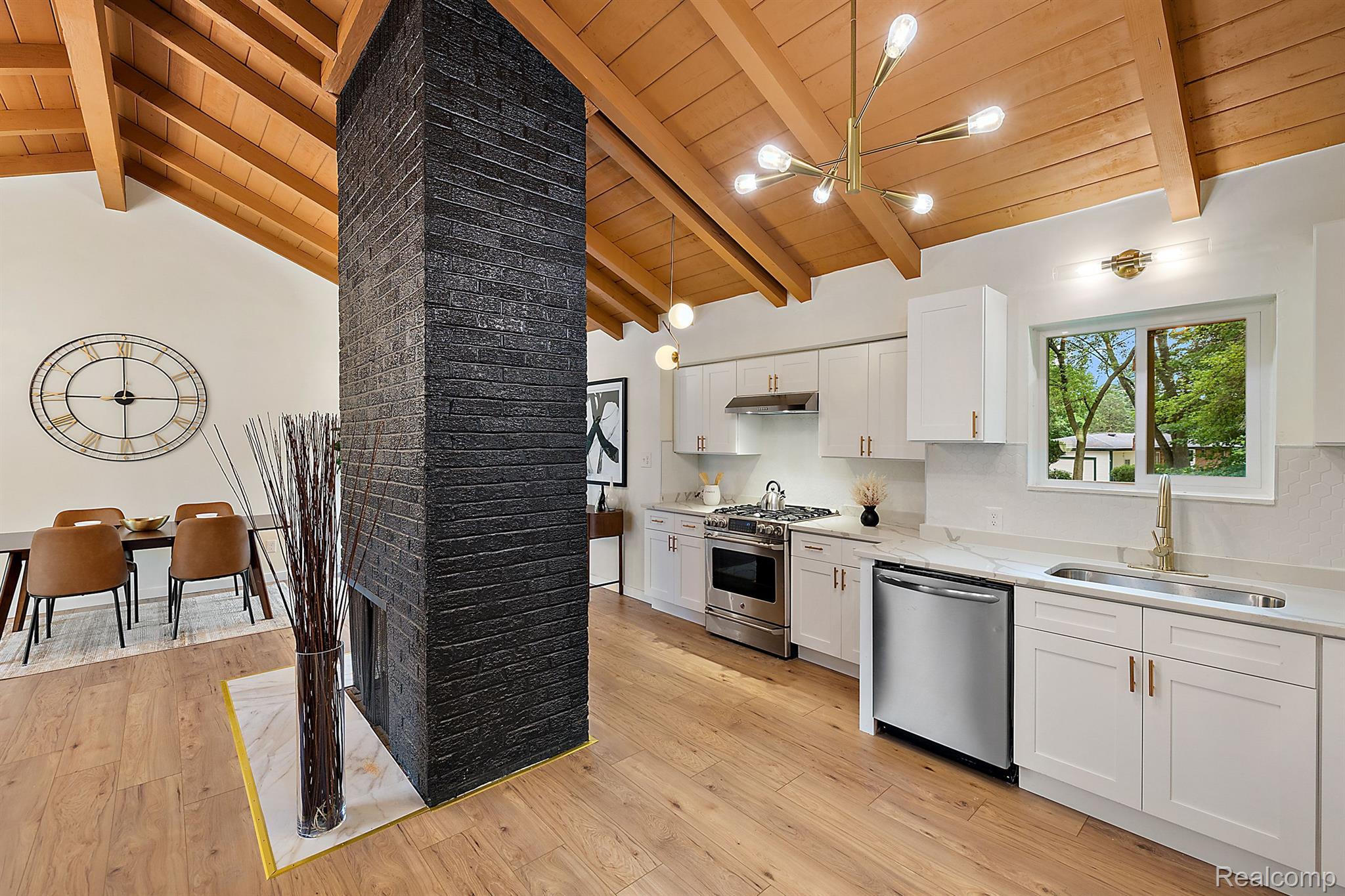 Open kitchen and dining area with a black brick fireplace and vaulted wood ceiling.