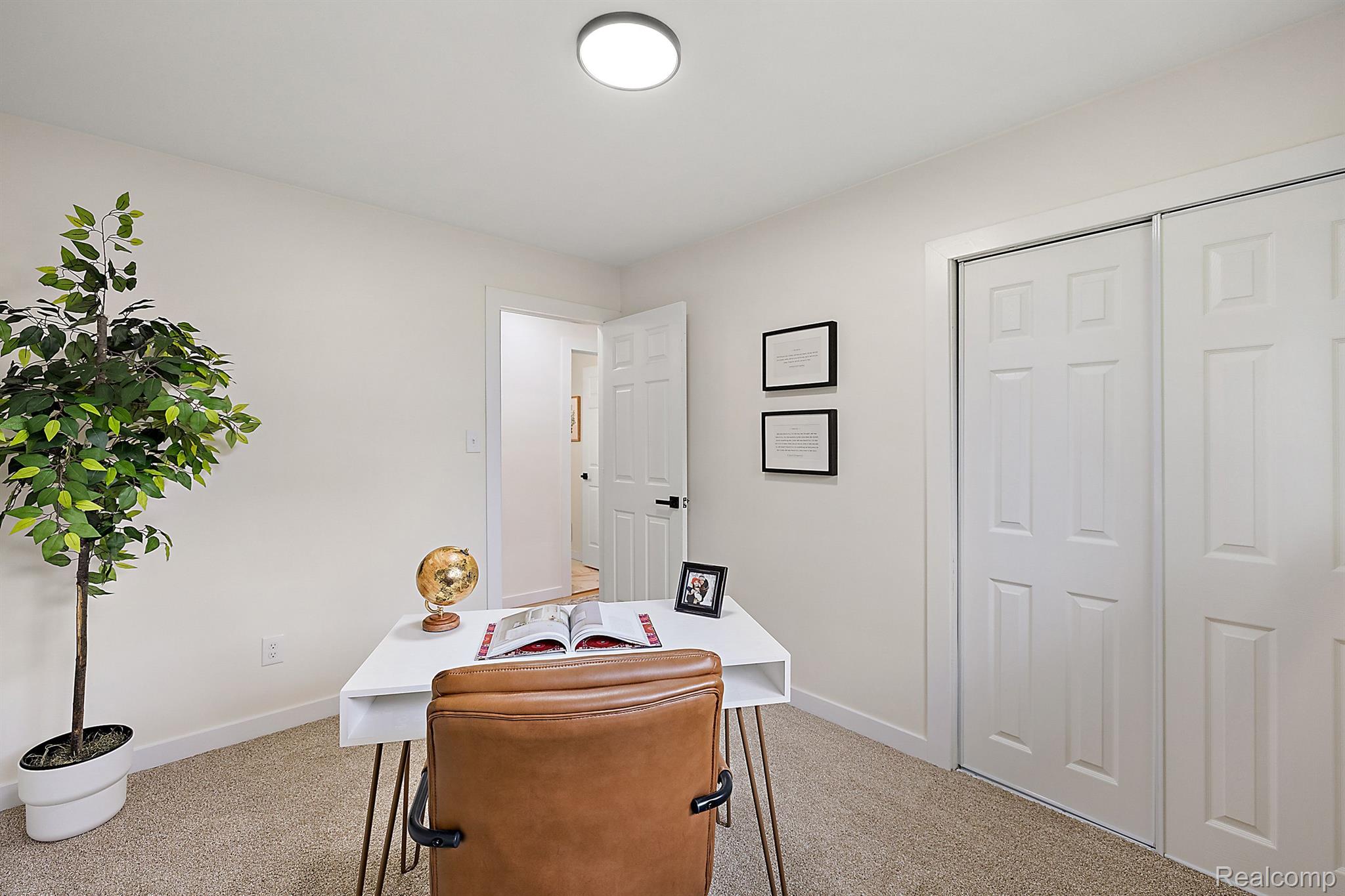 Home office with a white desk, tan leather chair, potted tree, and white closet doors.
