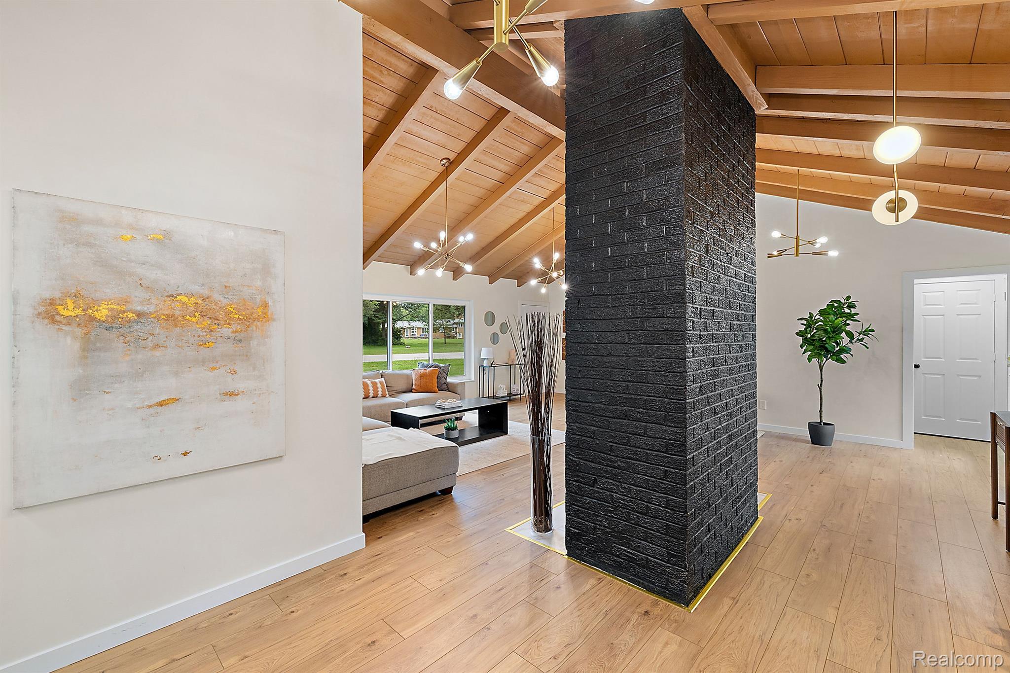 Open-plan living room with vaulted wood ceiling, hardwood floors, and a striking black brick chimney.