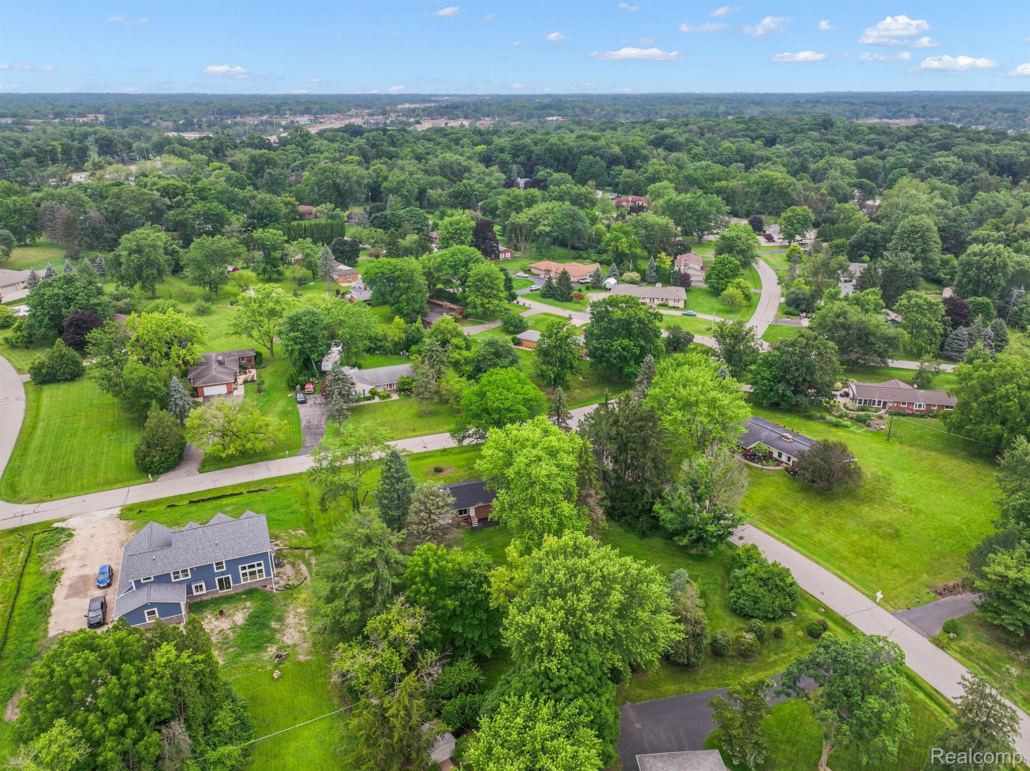 Aerial view of leafy homes and curving streets, with a blue-gray house prominent in the foreground.