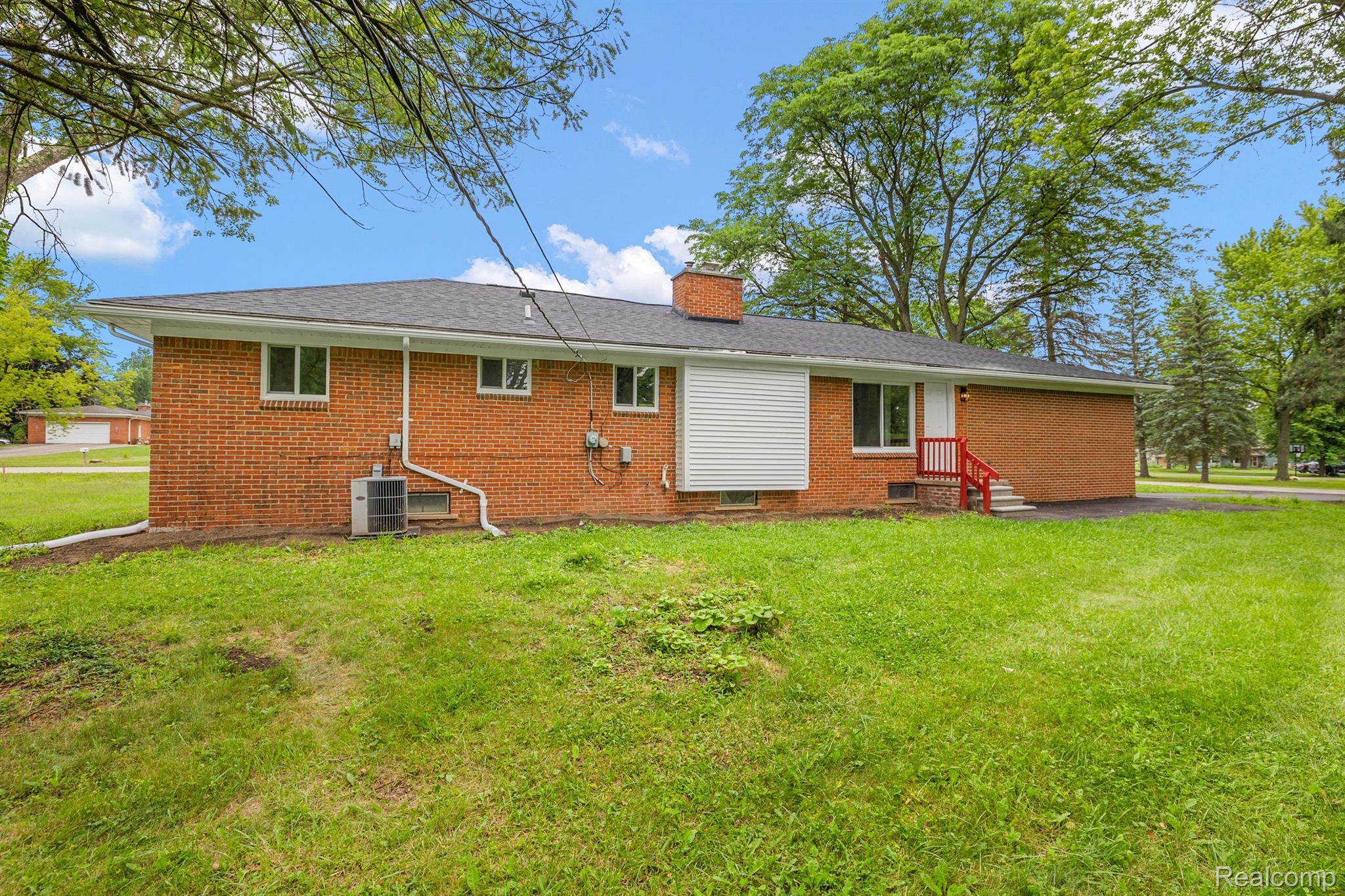 Single-story brick house with red entry steps and a broad lawn shaded by mature trees.