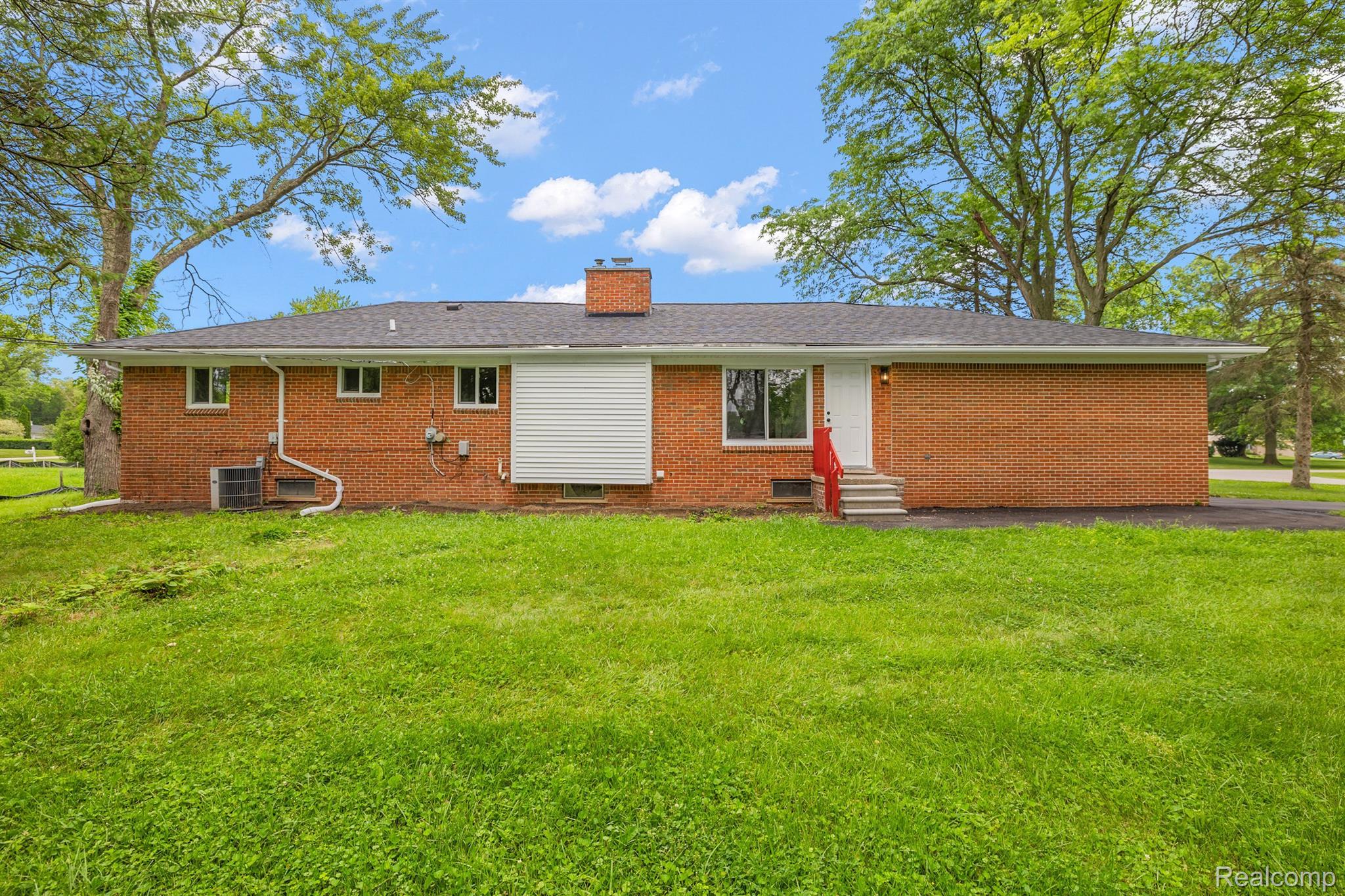 Single-story brick house with a white rear door, steps, and broad green lawn.
