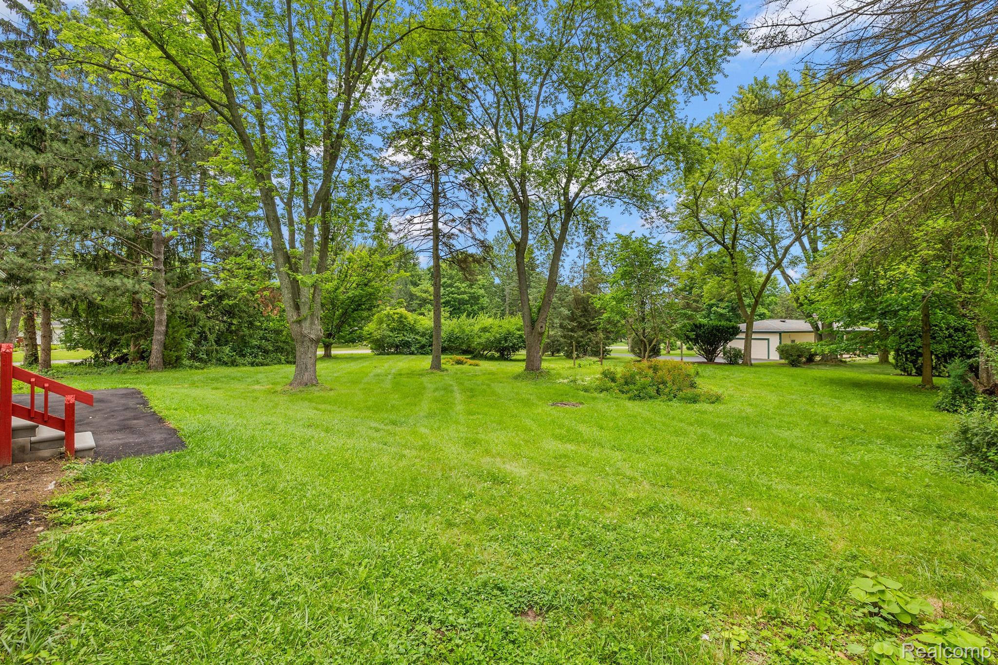 Grassy backyard with mature trees, red deck steps, and a detached garage.