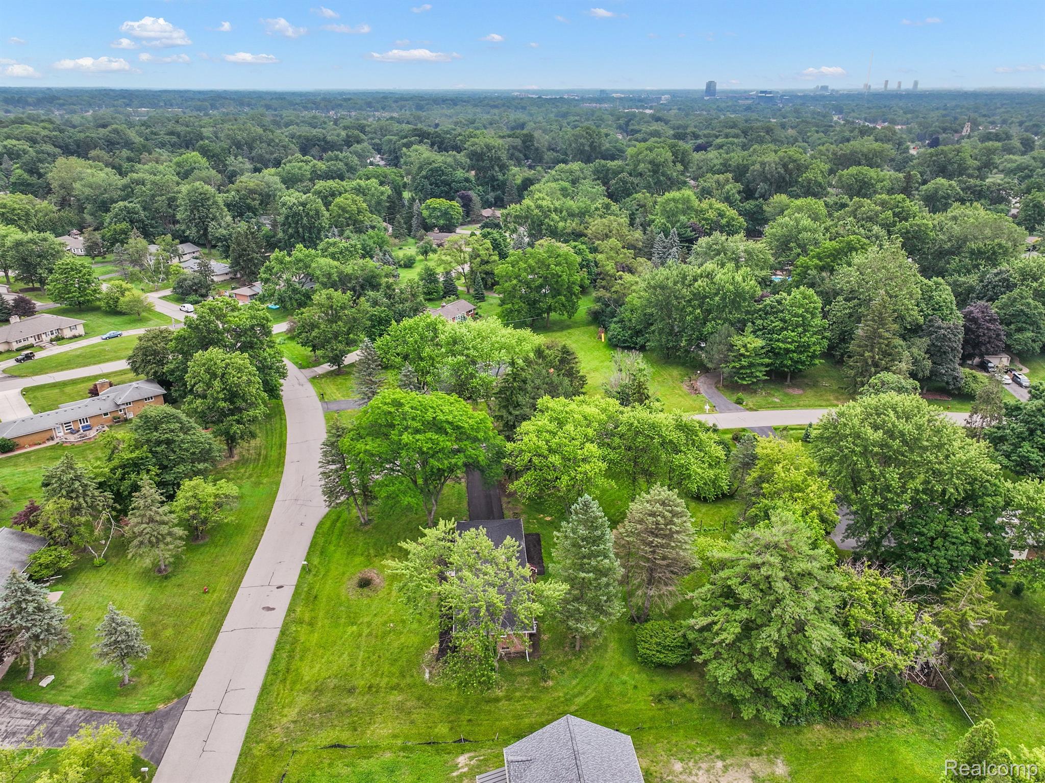 Aerial view of a wooded neighborhood with detached homes and a curving residential street.