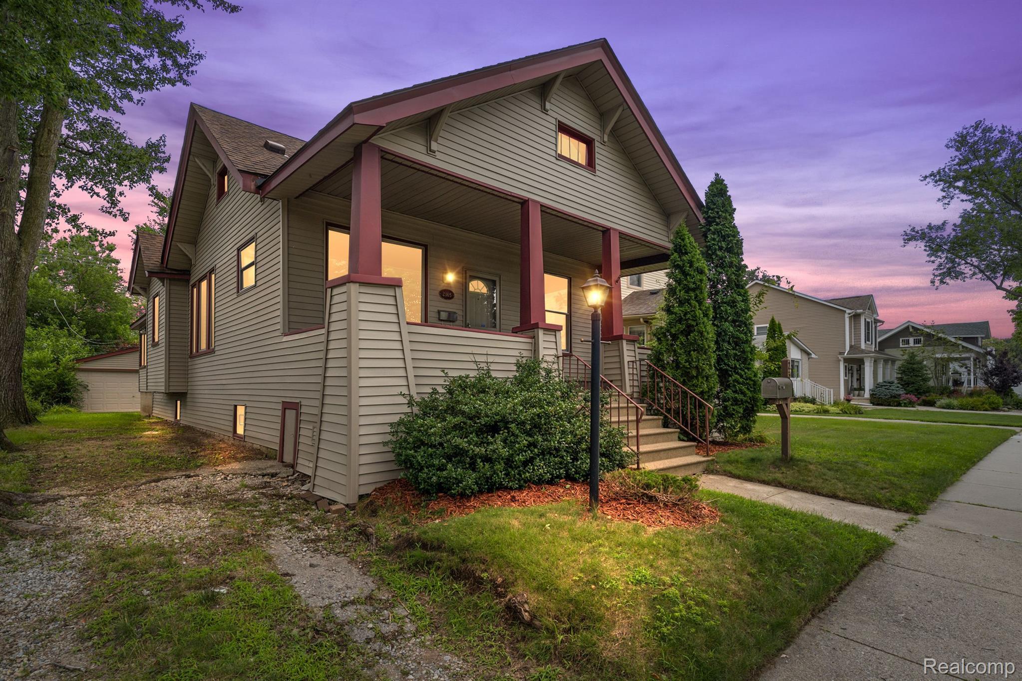 Gray two-story home with burgundy porch trim and illuminated windows at dusk.