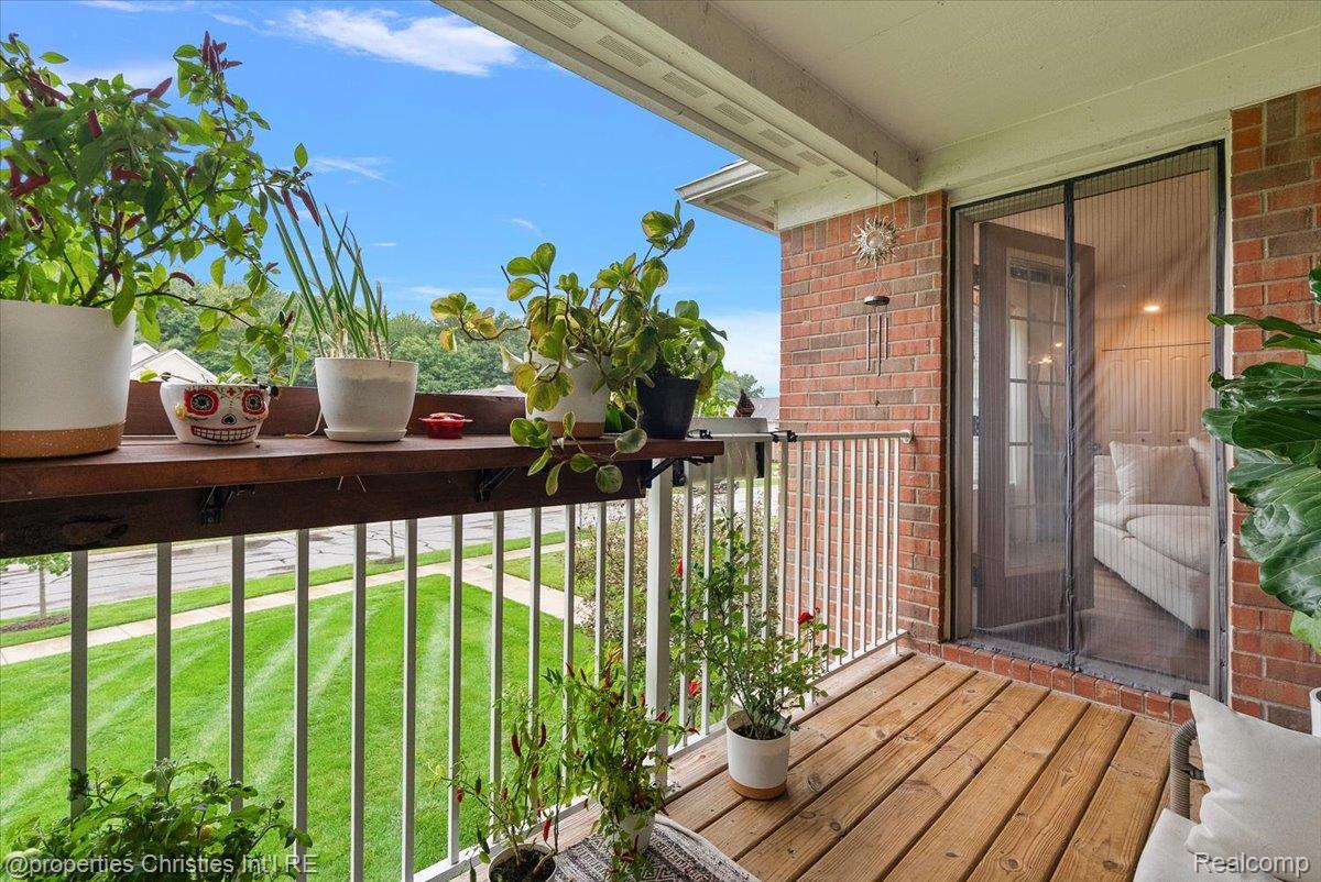 Covered balcony with wooden decking, potted plants, and a view over the lawn.
