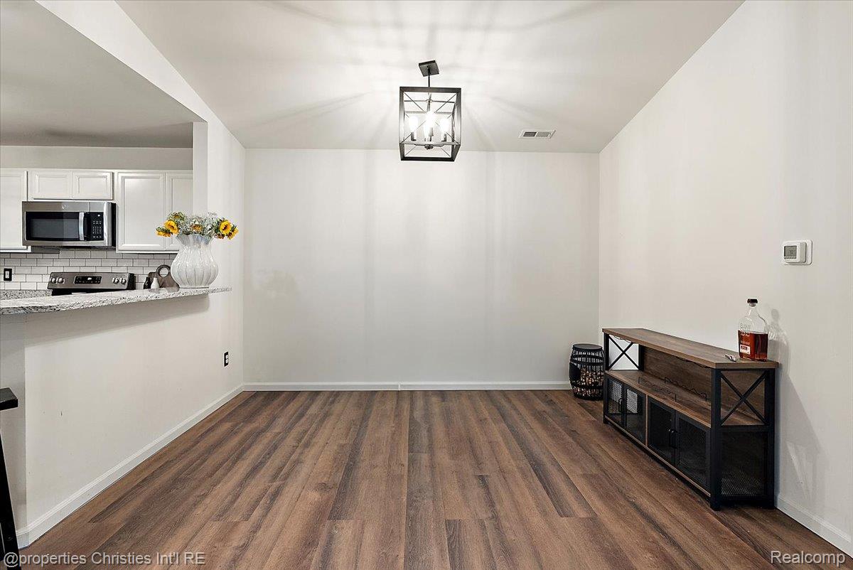 Dining area with wood-look floors and a geometric pendant, open to a white kitchen.