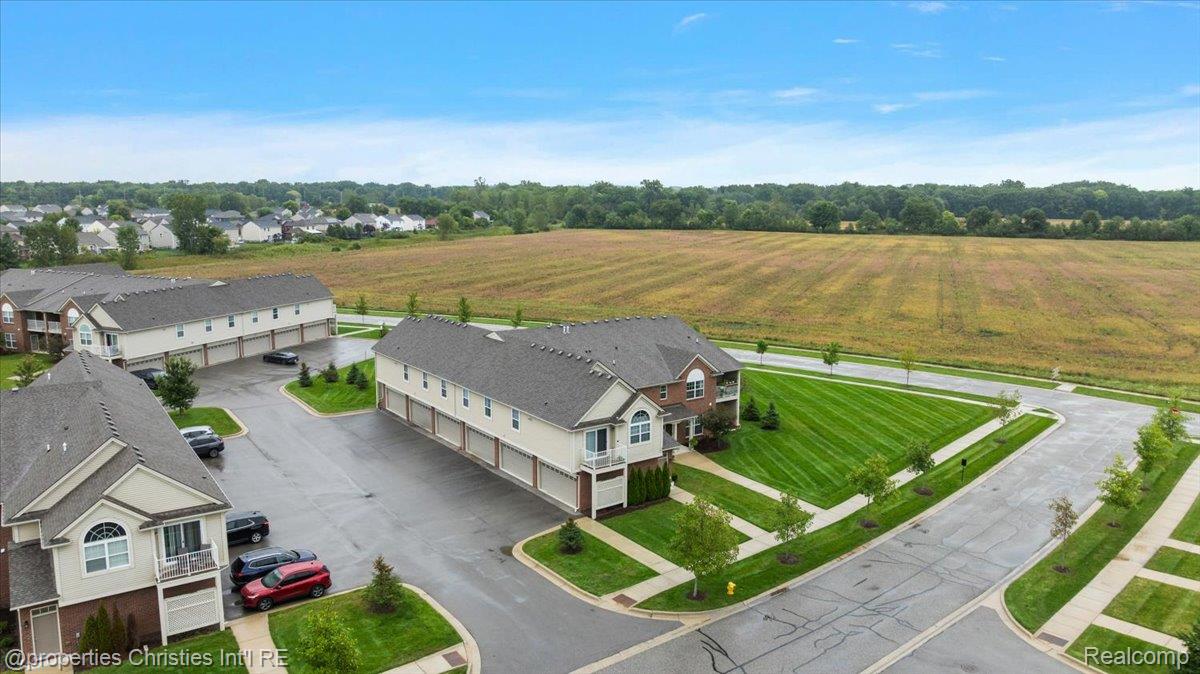 Aerial view of condominium buildings beside a broad open field, with parking and striped lawns.
