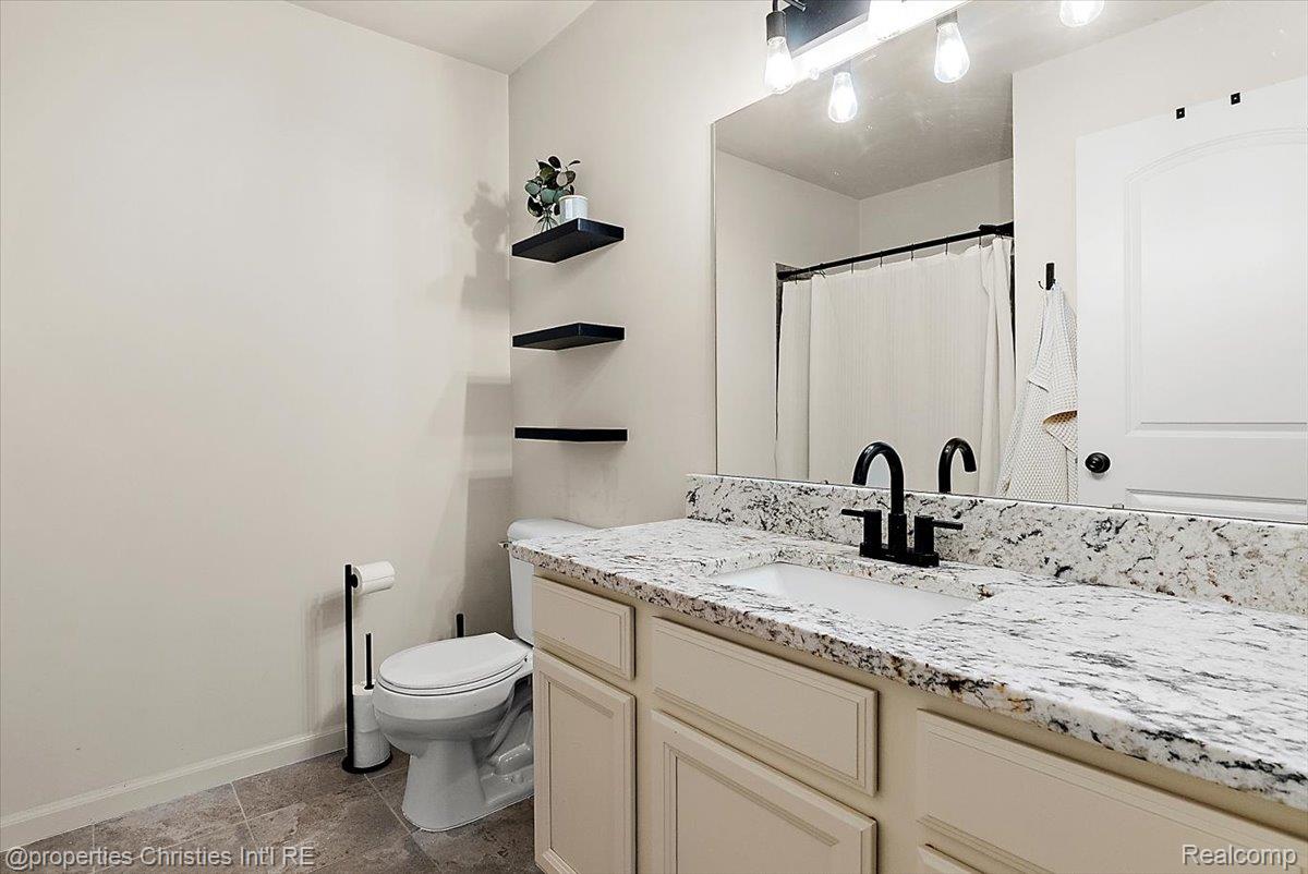 Bathroom with a marbled vanity countertop, black faucet, and three floating shelves beside a large mirror.