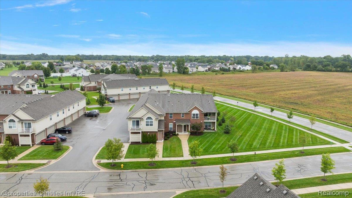 Aerial view of a brick-and-siding home, neighboring houses, landscaped lawns, and an open field.