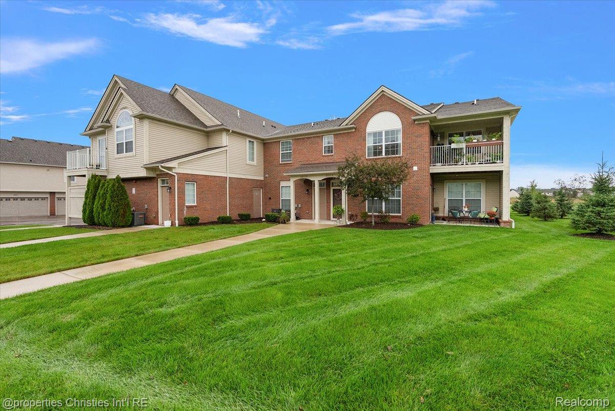 Two-story brick and beige residential building with balconies, a broad lawn, and a paved walkway.