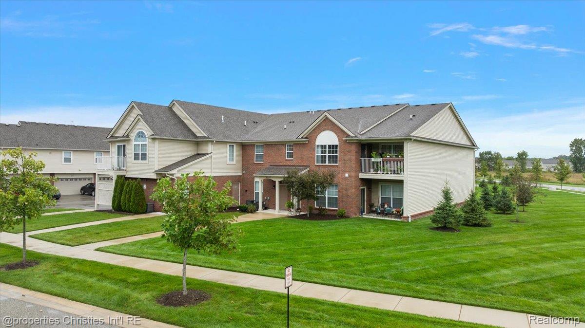 Multi-unit residence with brick and siding, balconies, and a broad green lawn.