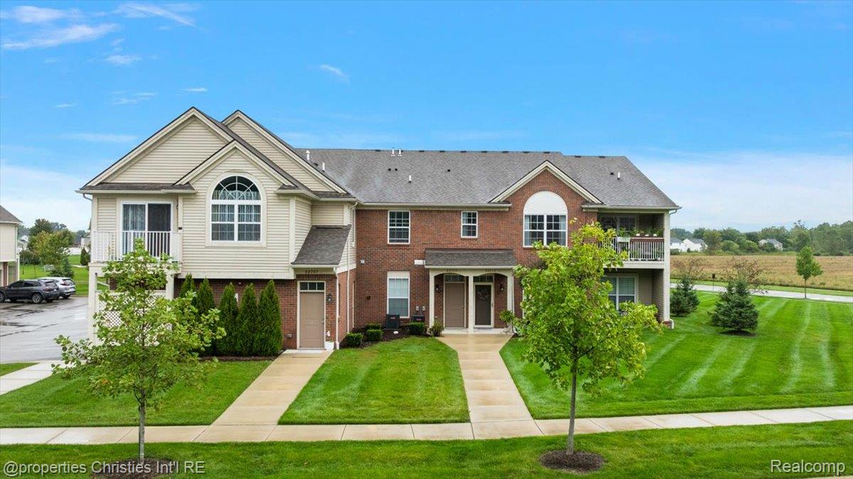 Residential building with brick and beige siding, arched windows, balconies, and a manicured lawn.