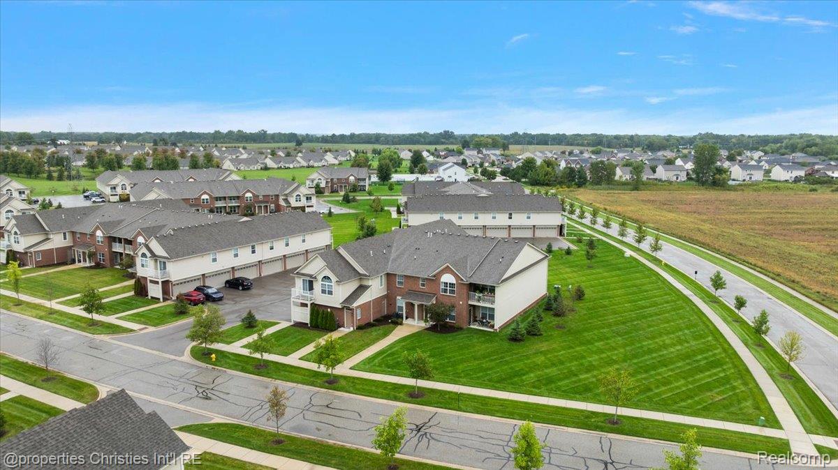 Aerial view of condominium buildings with manicured lawns and a curving road beside an open field.