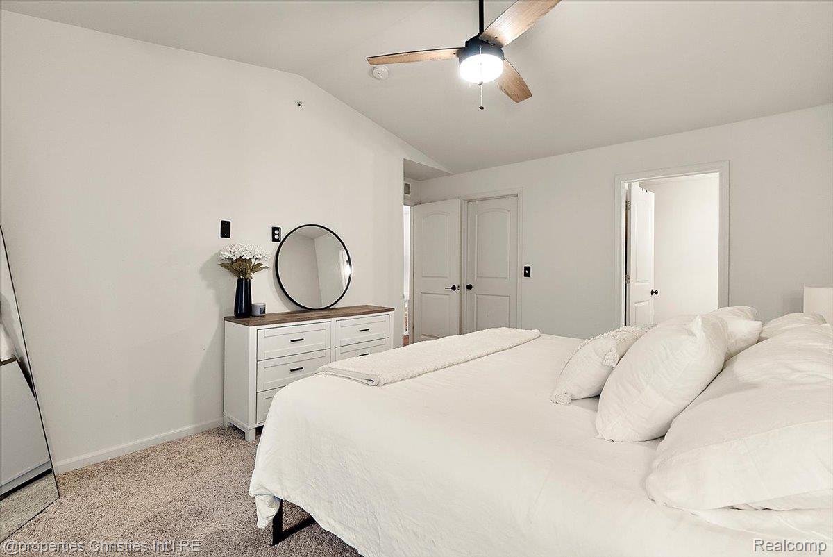 Bedroom with a white bed, carpeted floor, dresser and round mirror, and ceiling fan.