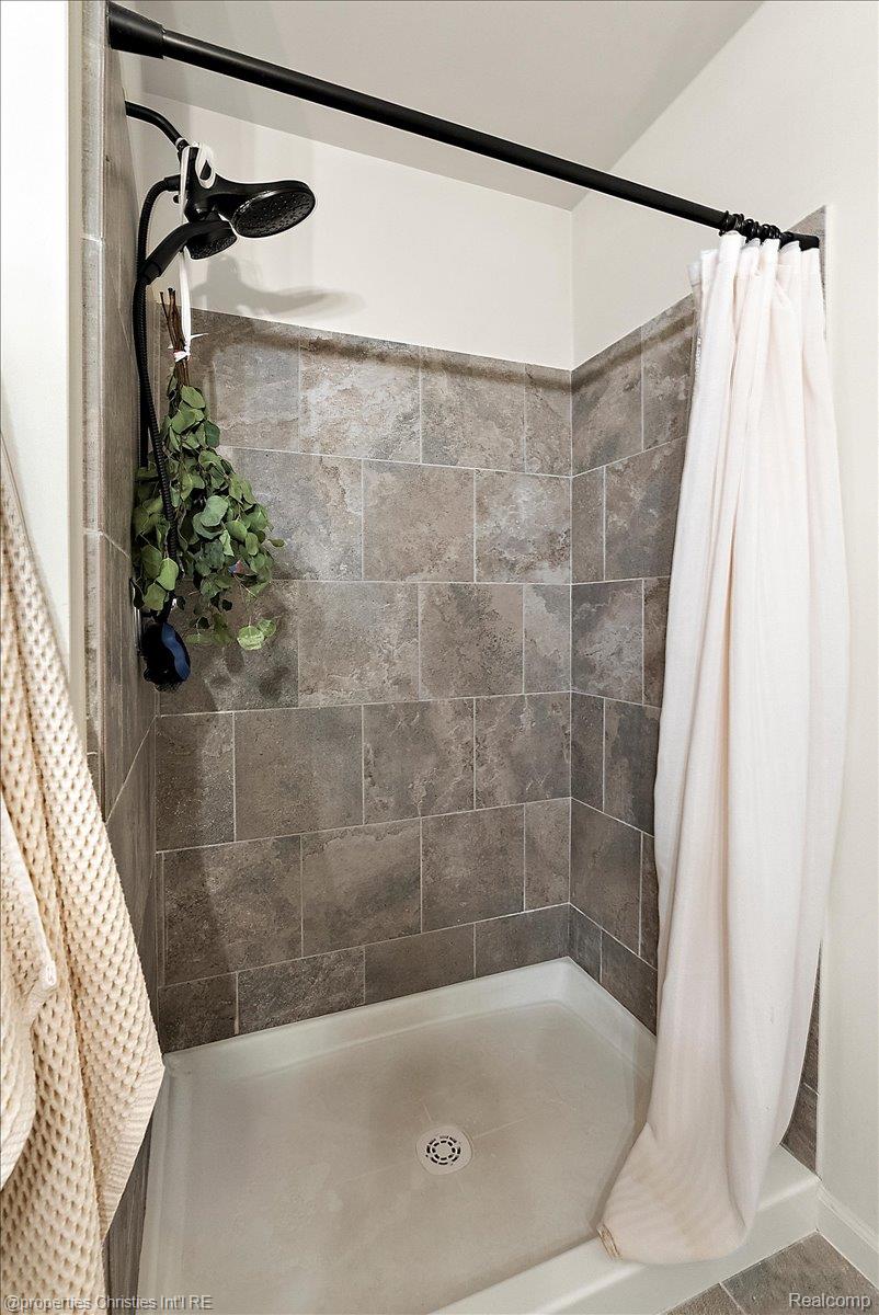 Bathroom shower with gray tile walls, black fixtures, and a white curtain.