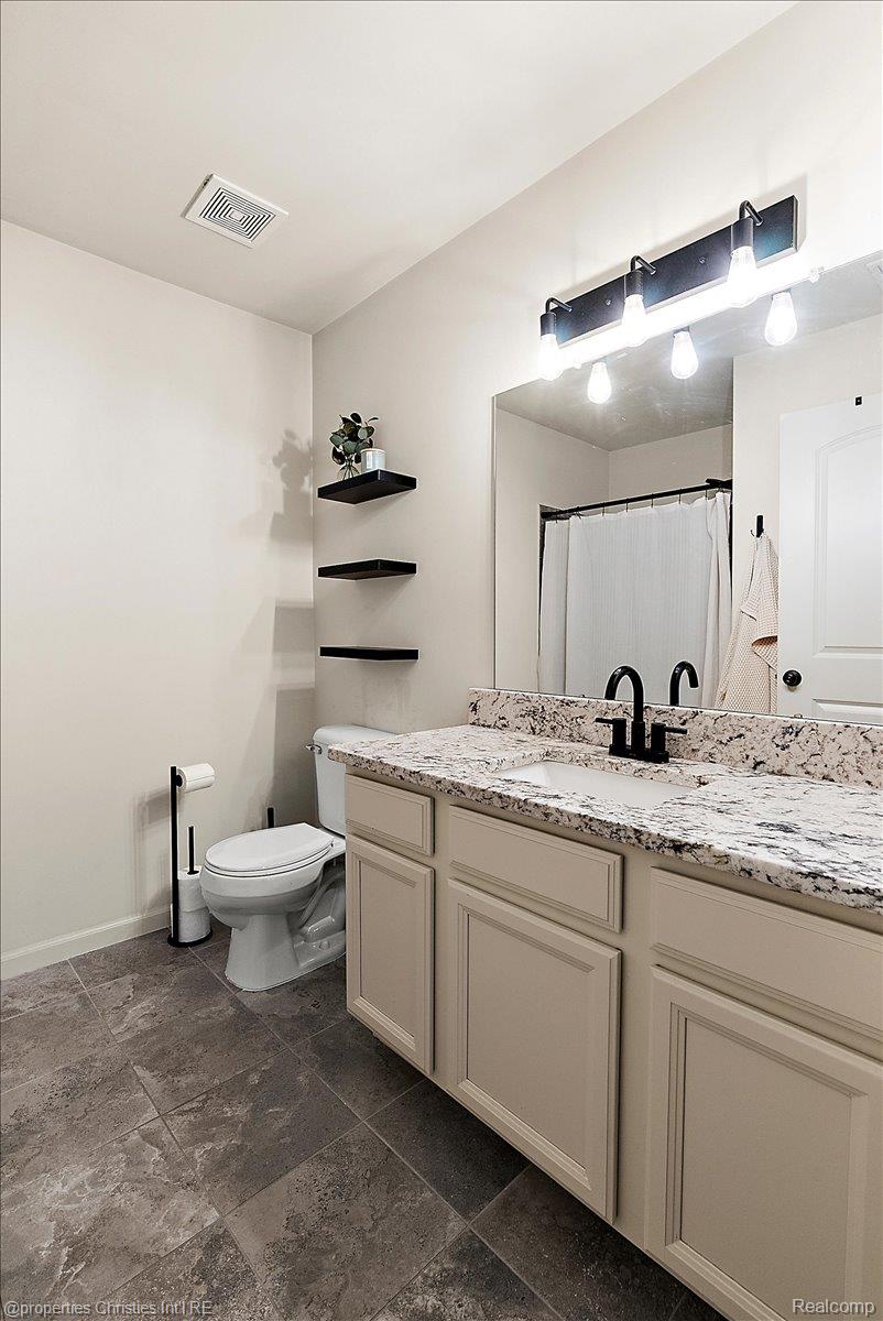 Bathroom with a granite vanity, black faucet, large mirror, and dark tile floor.