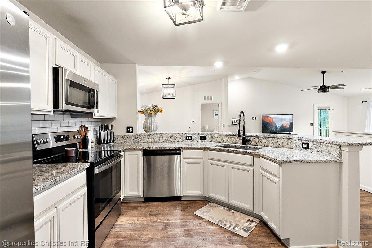 Open-plan kitchen with white cabinets, granite counters, stainless steel appliances, and a large peninsula.