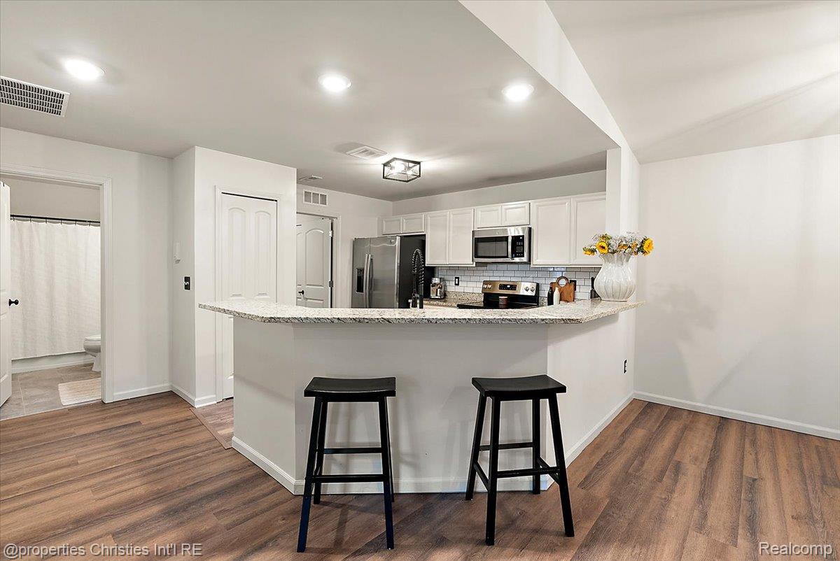Kitchen with white cabinets, stainless appliances, and a curved granite peninsula with two black stools.