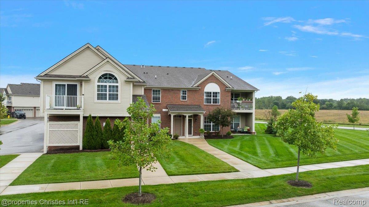 Two-story brick and beige-sided home with arched windows, balconies, and a landscaped lawn.