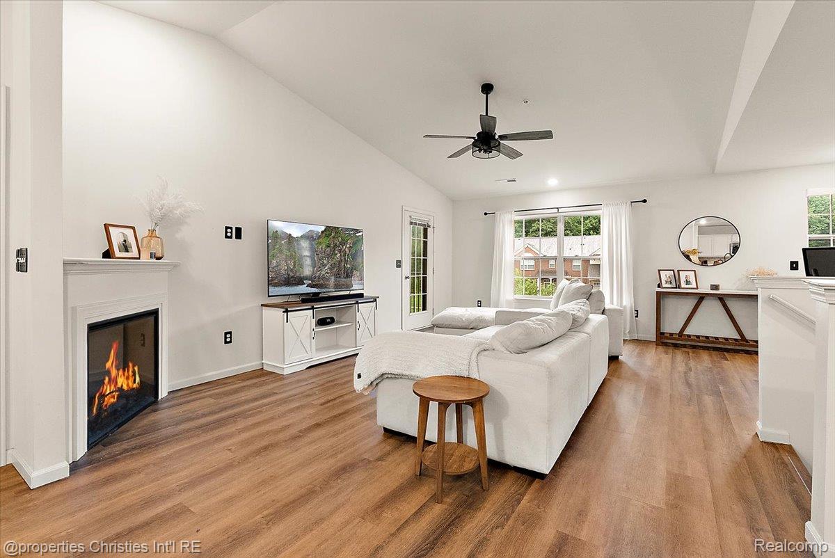 Staged living room with a white sectional, lit fireplace, television, and warm wood-look flooring.