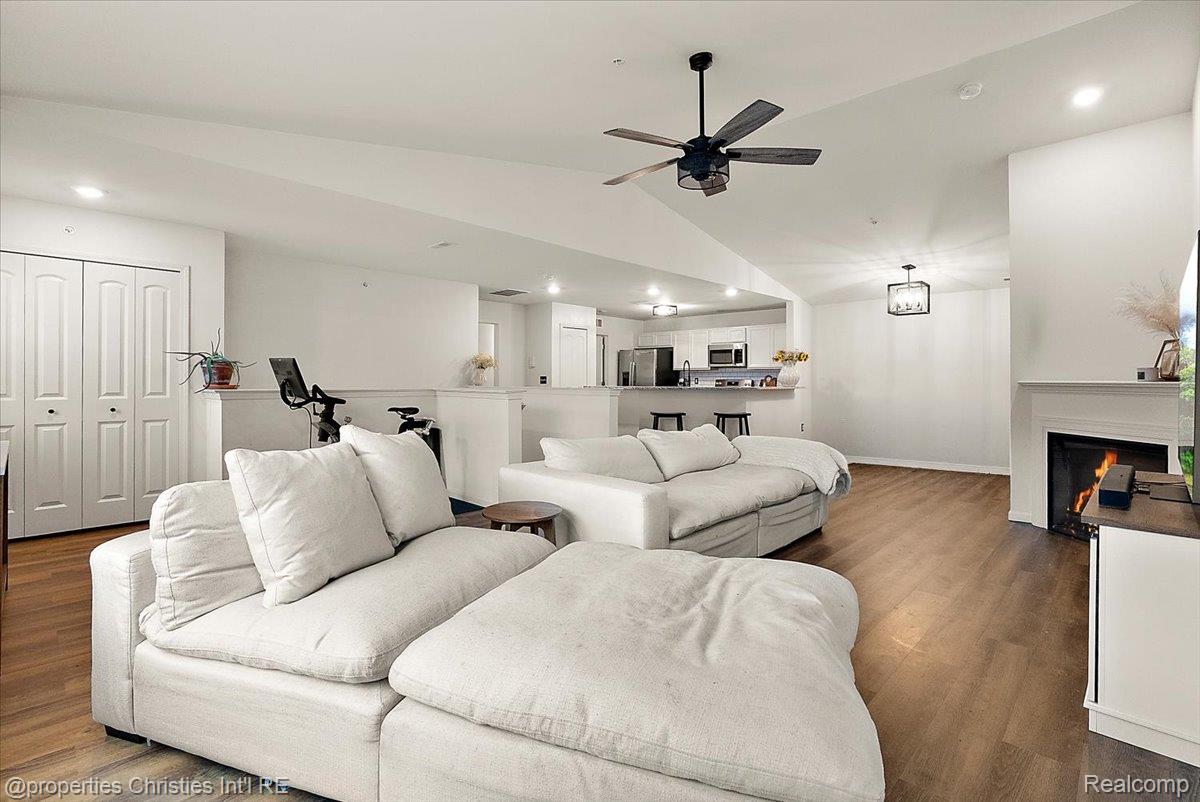 Open-plan living room with white sectional sofas, wood floors, and a fireplace beside the kitchen.