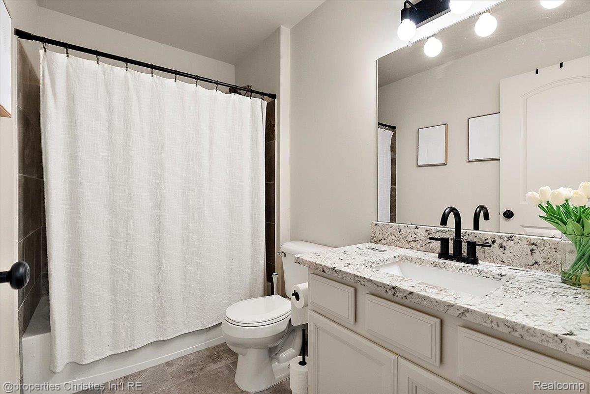 Bathroom with granite vanity, black faucet, white shower curtain, and tulips.