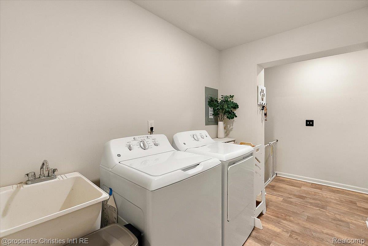 Laundry room with washer, dryer, deep utility sink, and wood-look flooring.